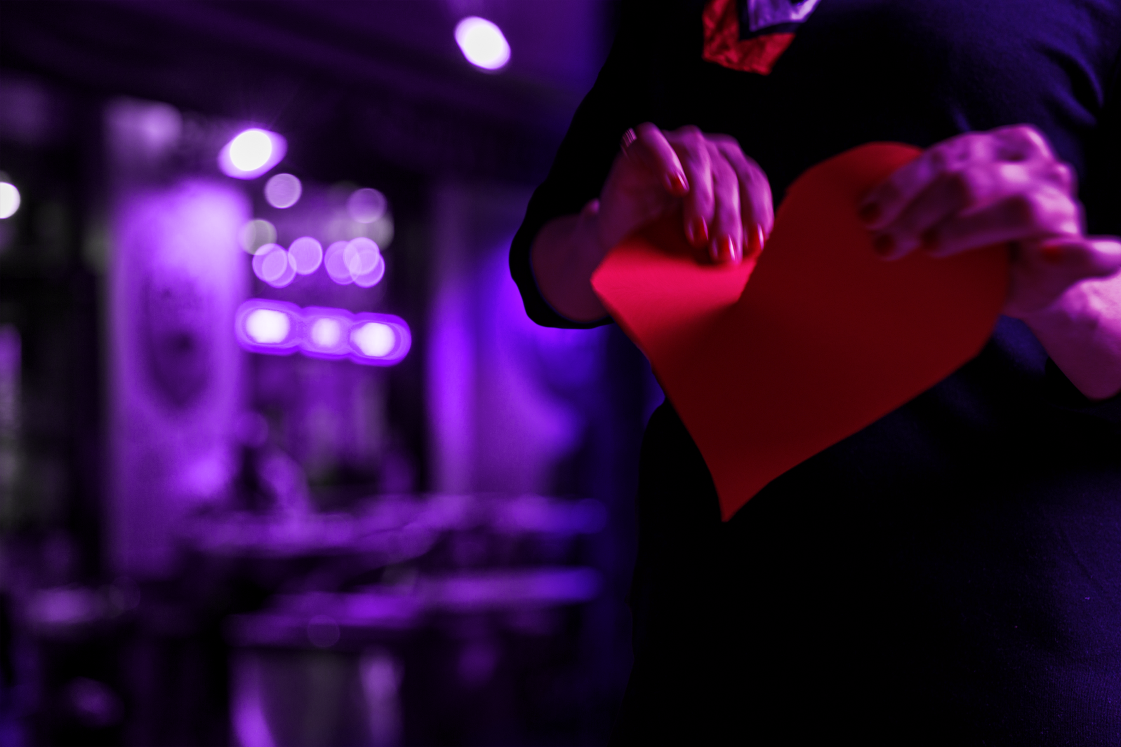 A person rips a red paper heart in half.