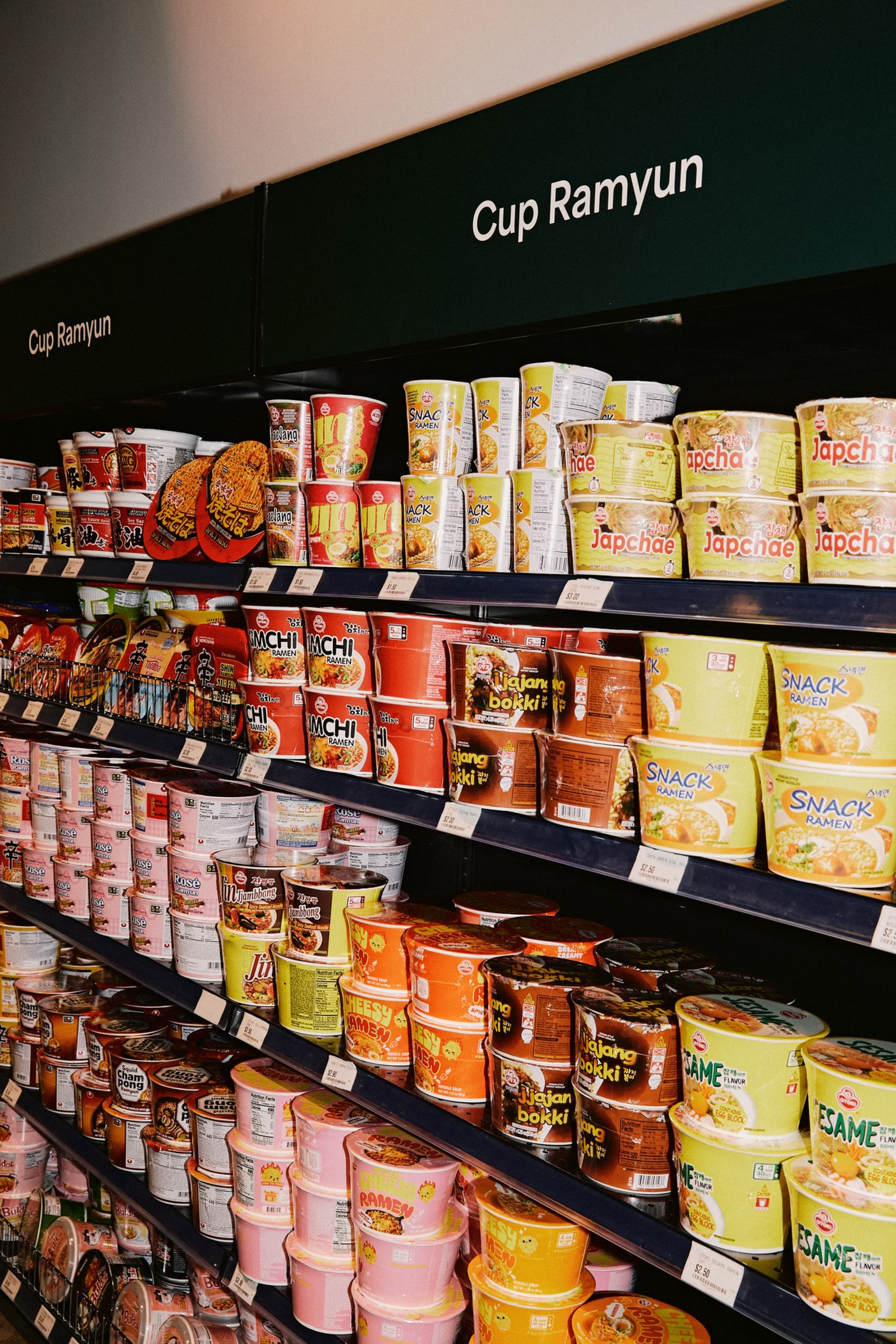 Shelves filled with various brands and flavors of cup ramyun instant noodles in colorful packaging.