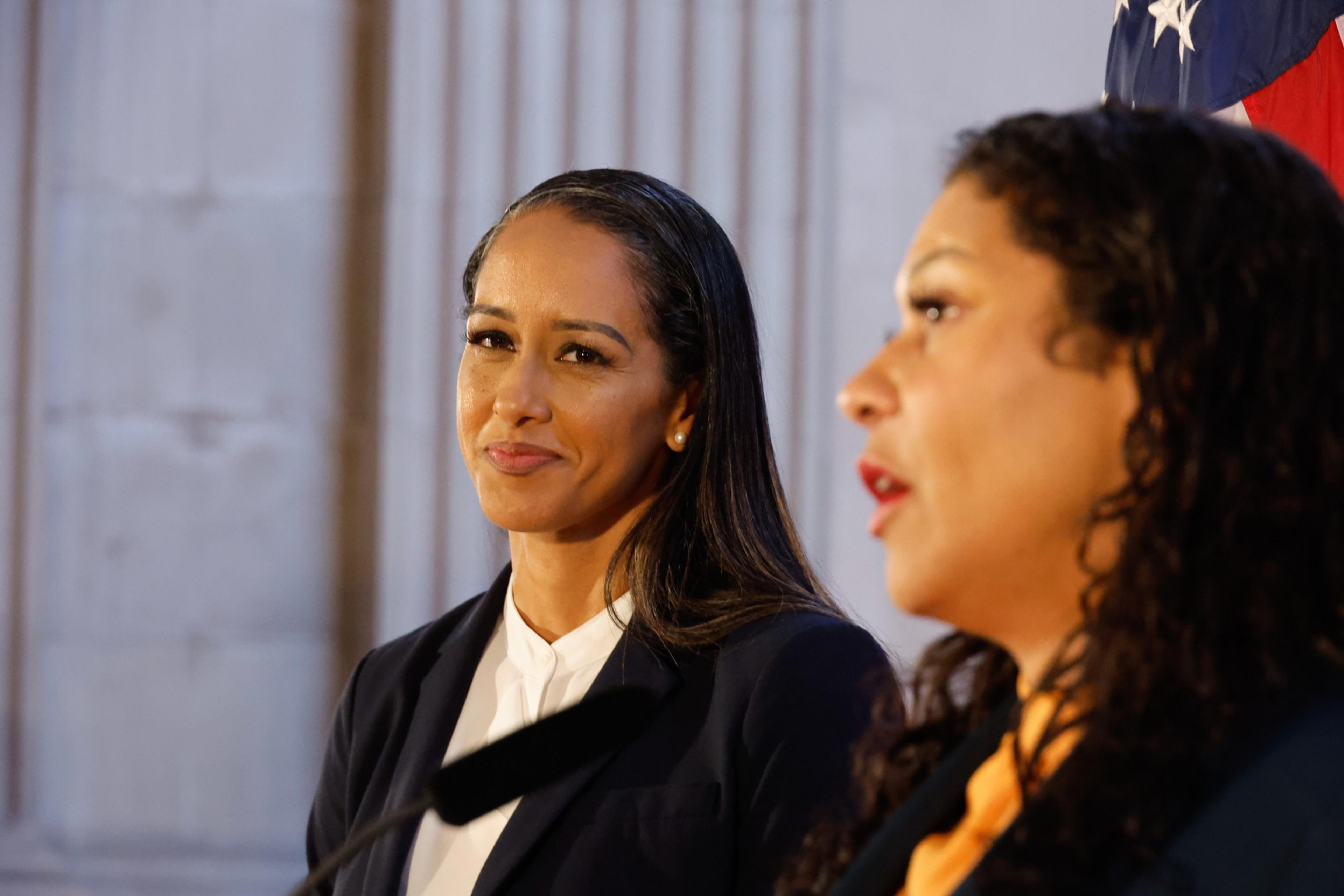 A woman in the foreground speaks while another woman in business attire smiles and listens attentively in a formal setting.