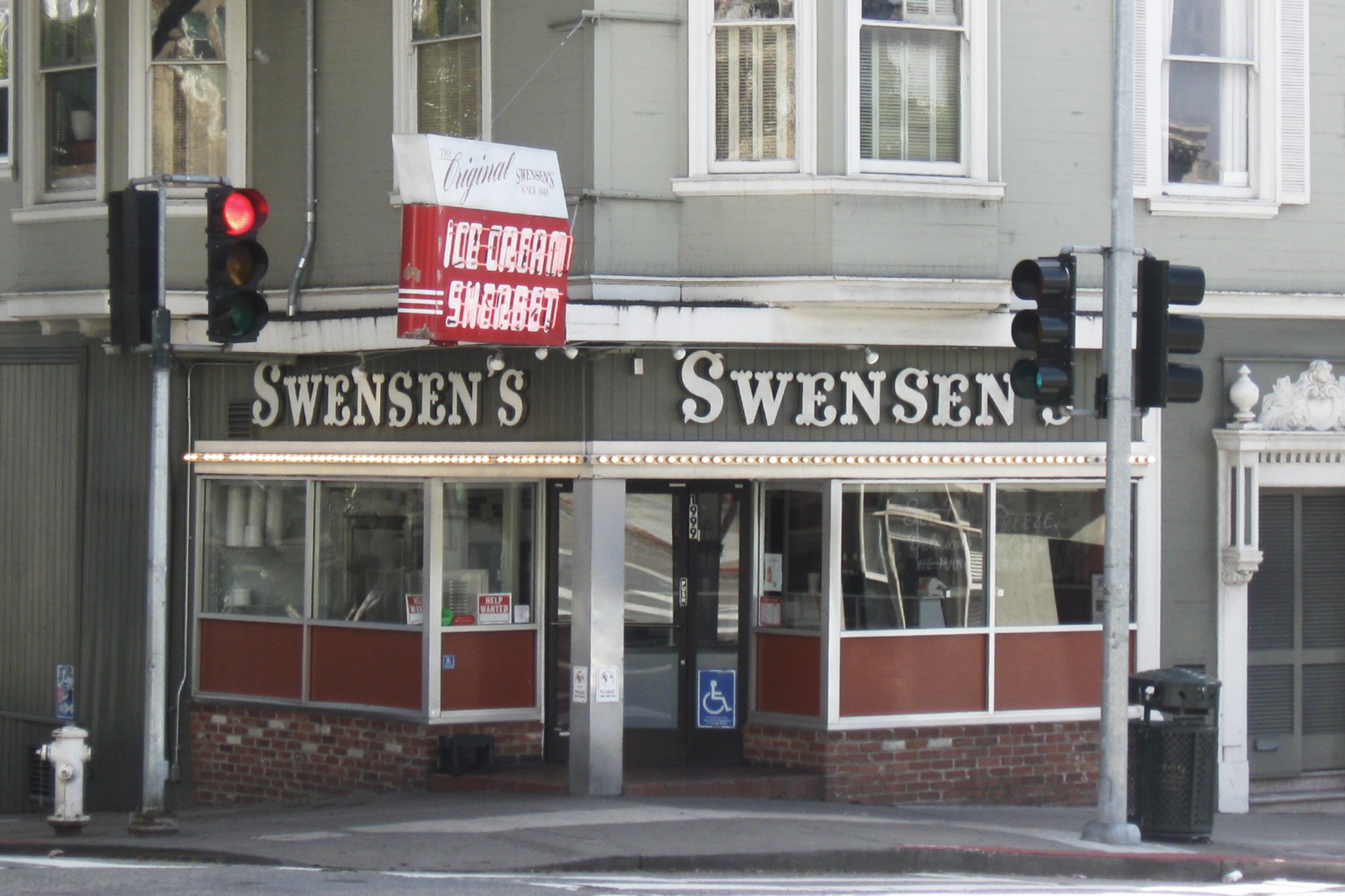 The image shows a corner shop with a sign reading &quot;Swensen's,&quot; featuring a vintage look with red and white accents, and a lit window display. There are traffic lights visible.