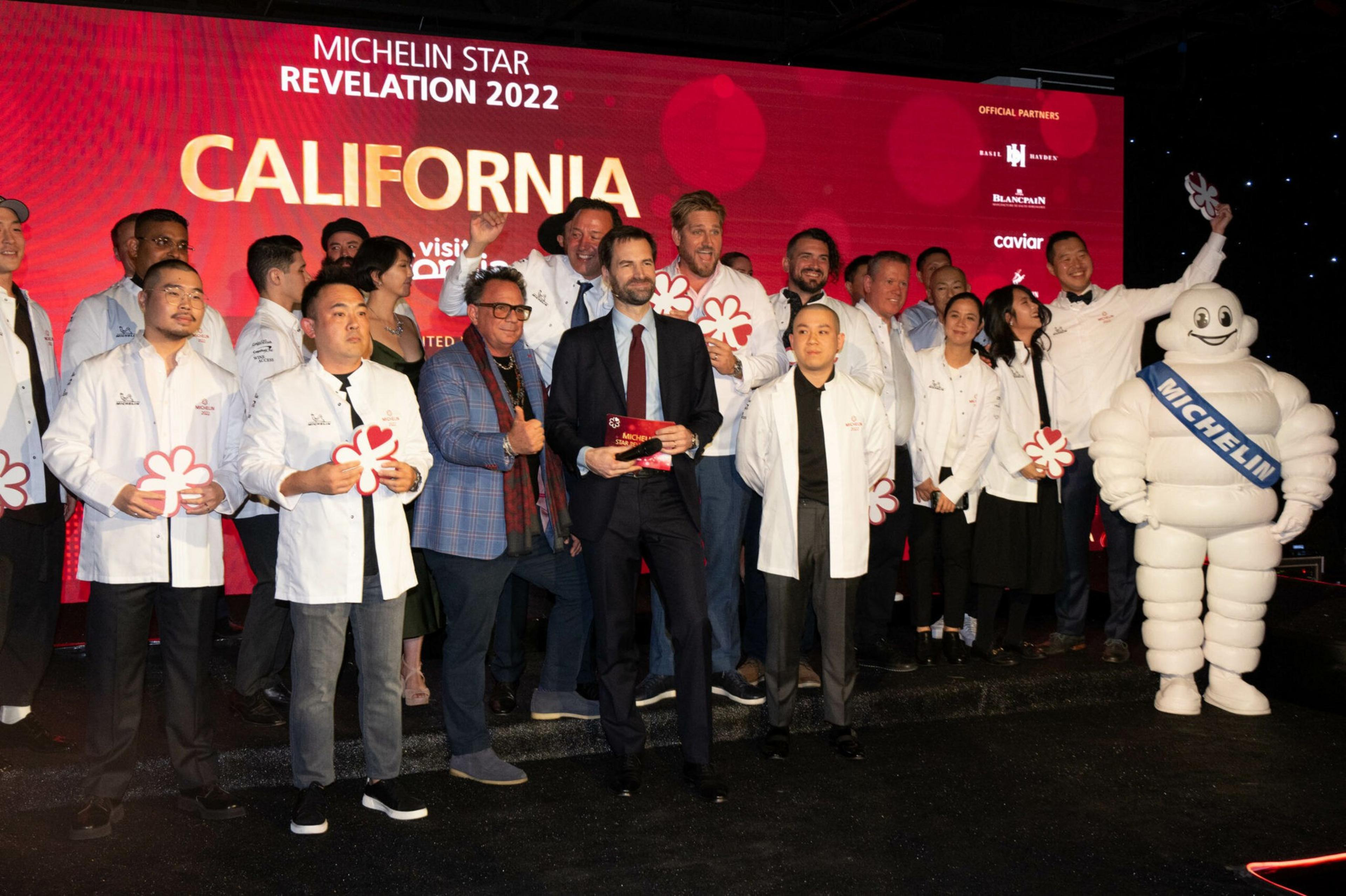 A group of chefs and guests pose on stage holding Michelin star awards, with the Michelin Man mascot on the right and a red "California Michelin Star Revelation 2022" backdrop.