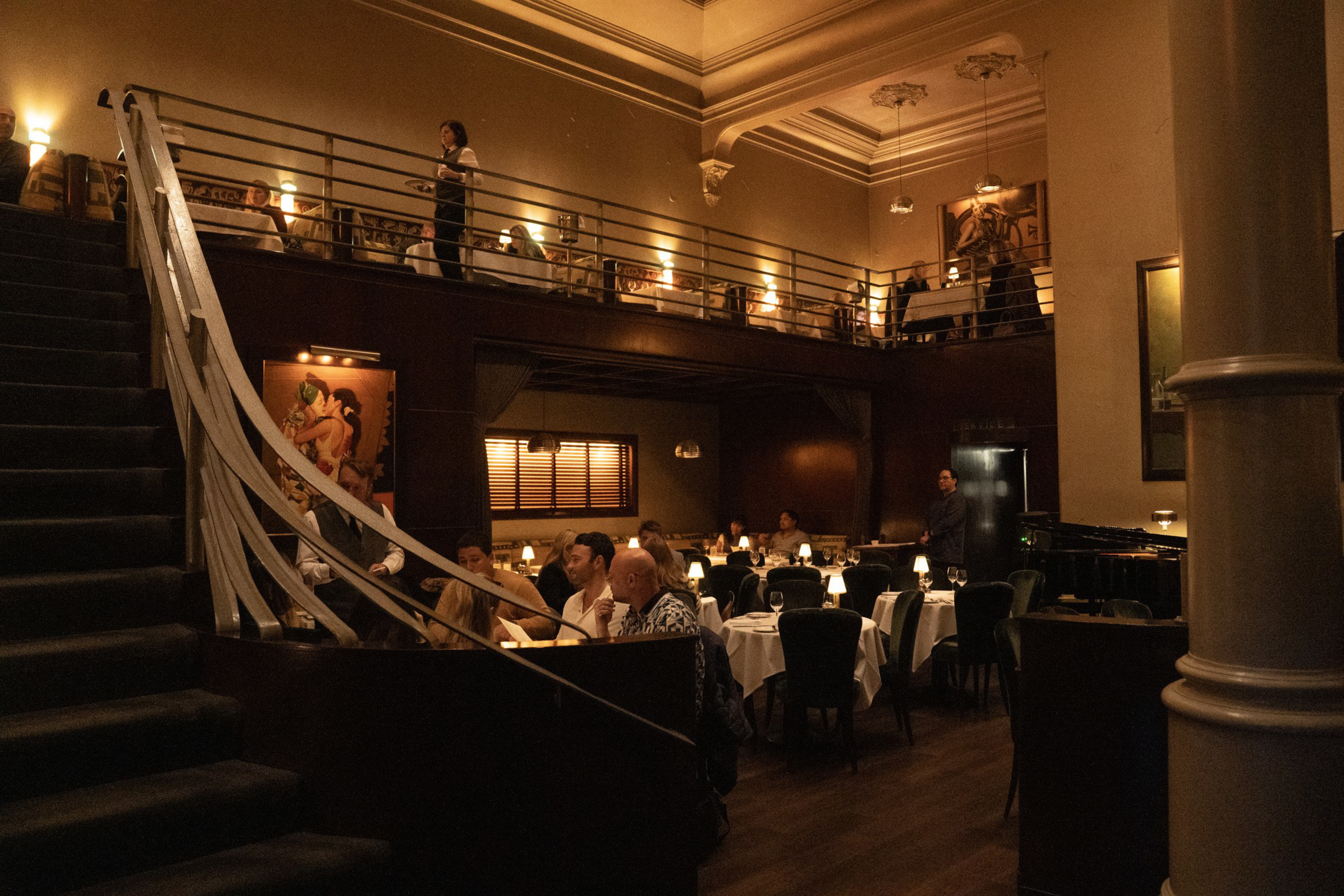 A dimly lit, elegant restaurant with a staircase wrapped in white tape, tables filled with diners, and cozy candlelit ambiance.