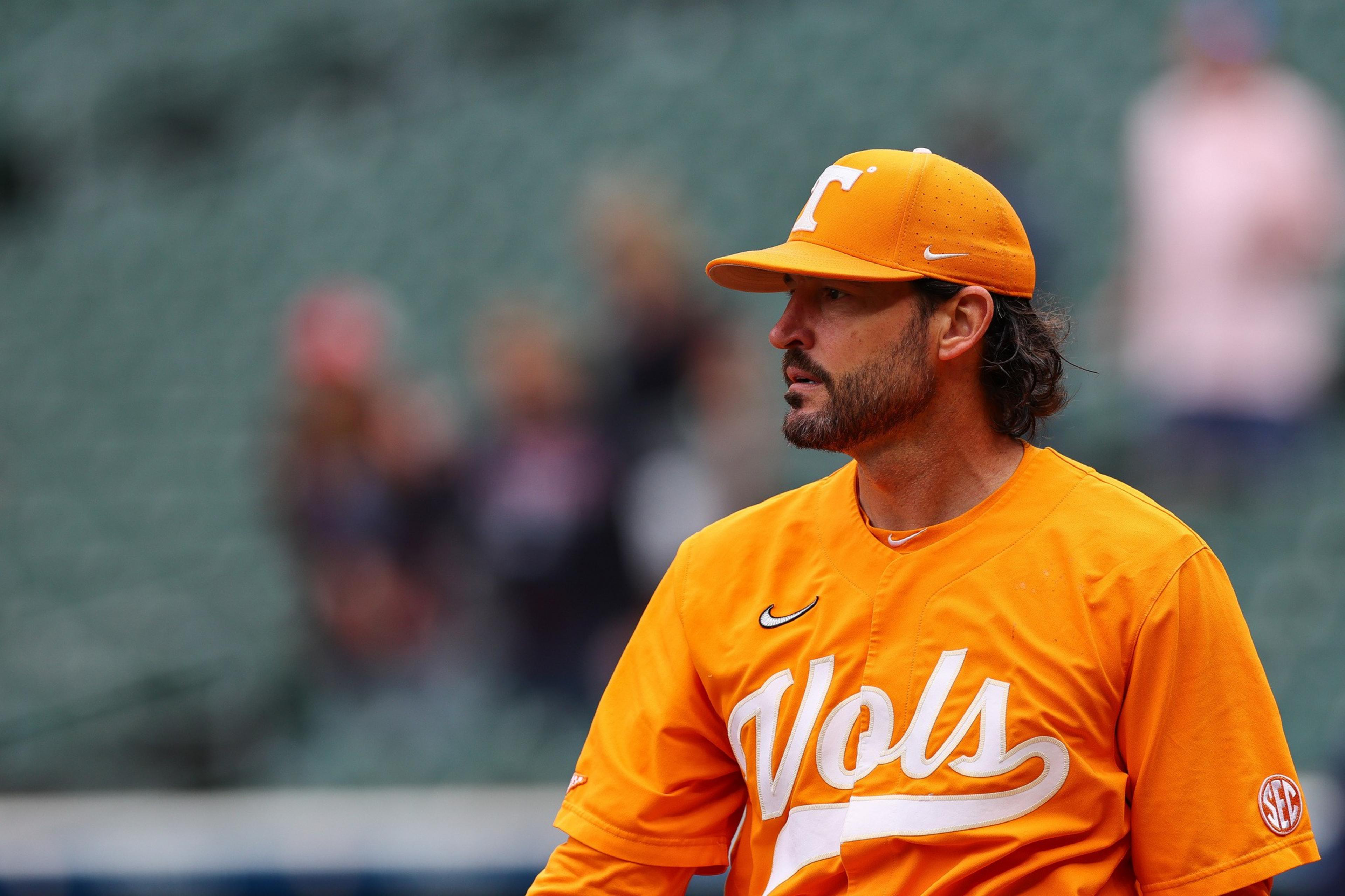 A man wearing an orange baseball uniform and cap with "Vols" written on the jersey stands looking to the side in a stadium with blurred spectators in the background.
