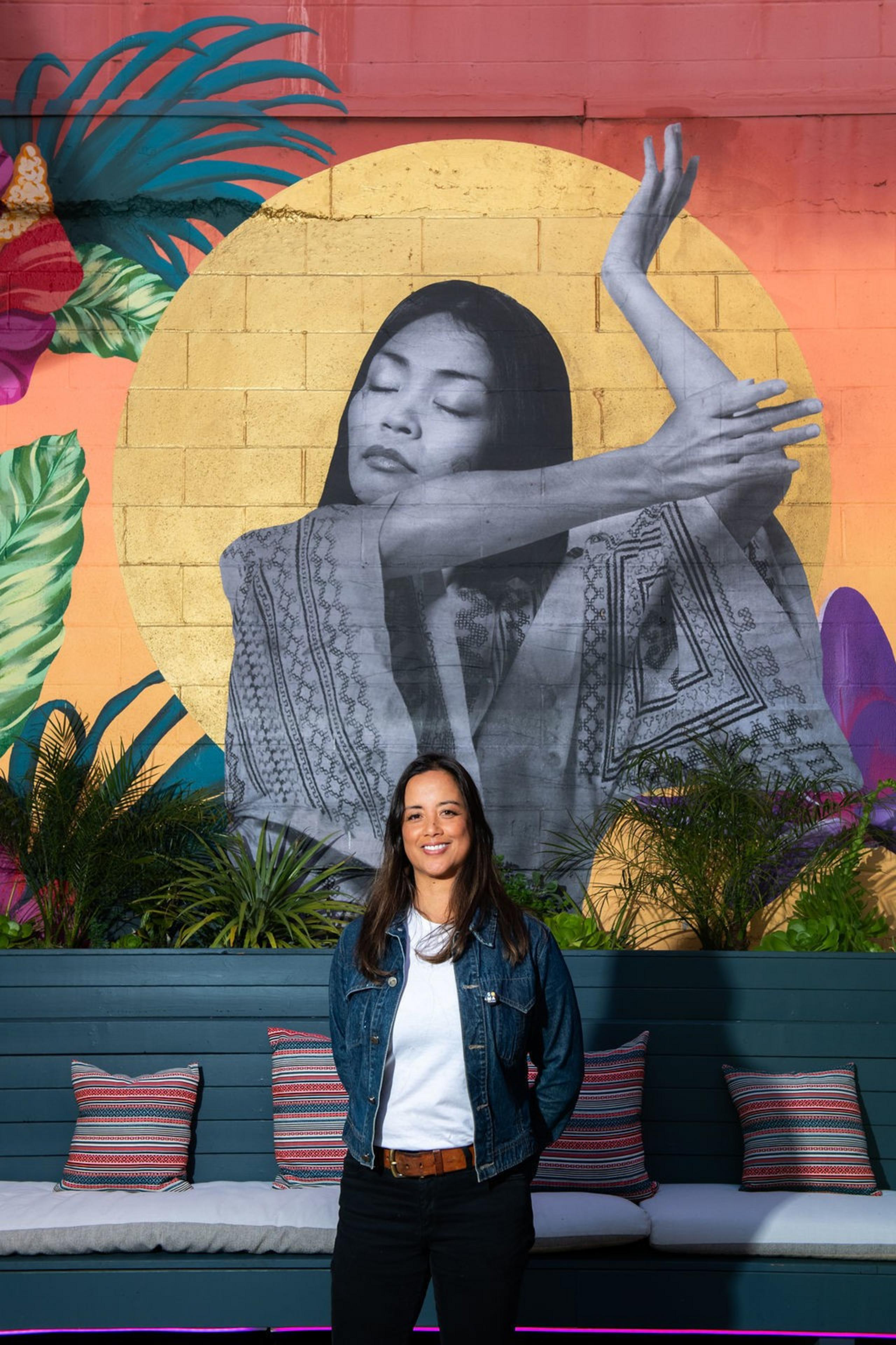a Filipina woman stands in front of a large mural depicting a Filpina woman