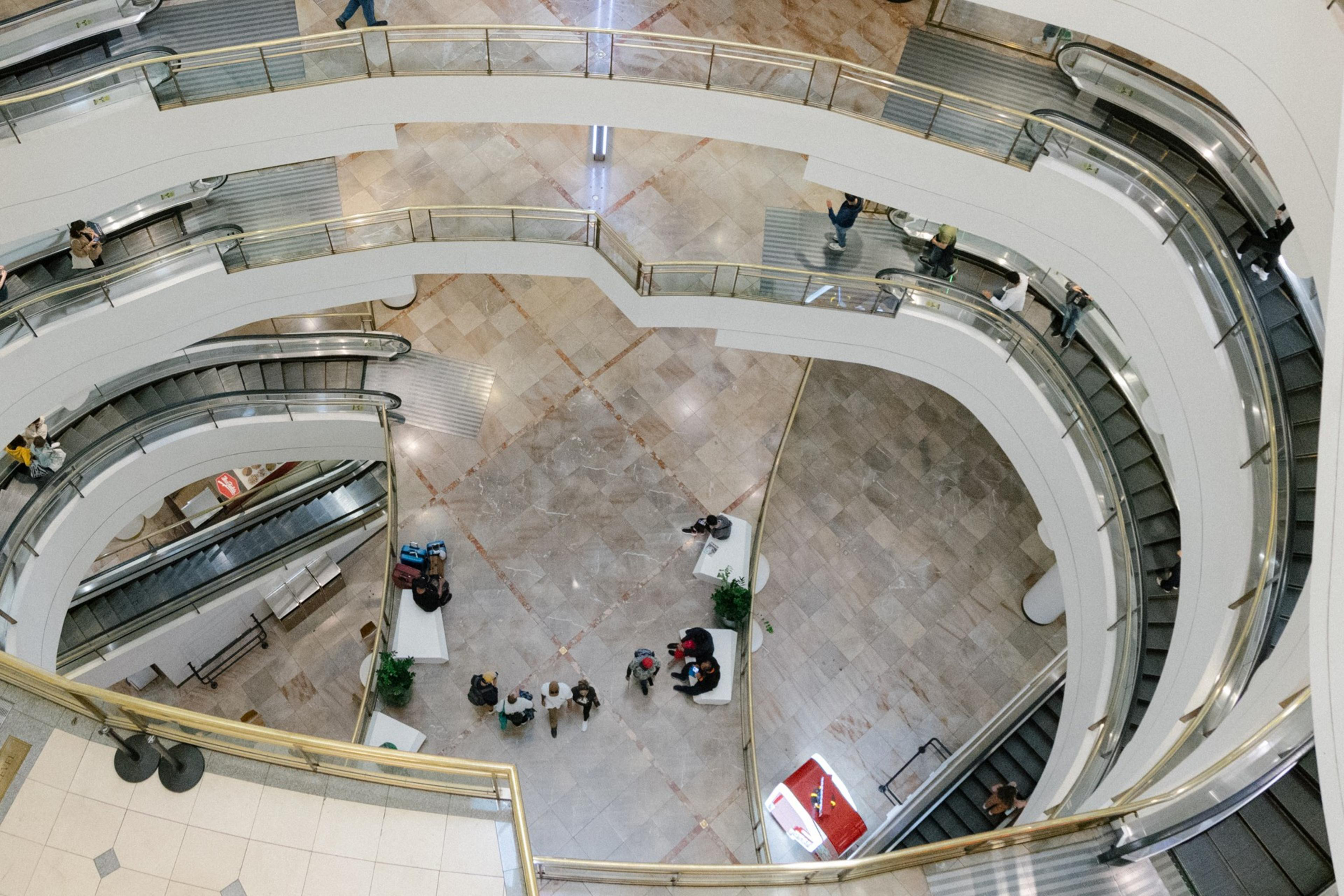 An overhead view of a multi-level shopping center with curving escalators and people milling about.