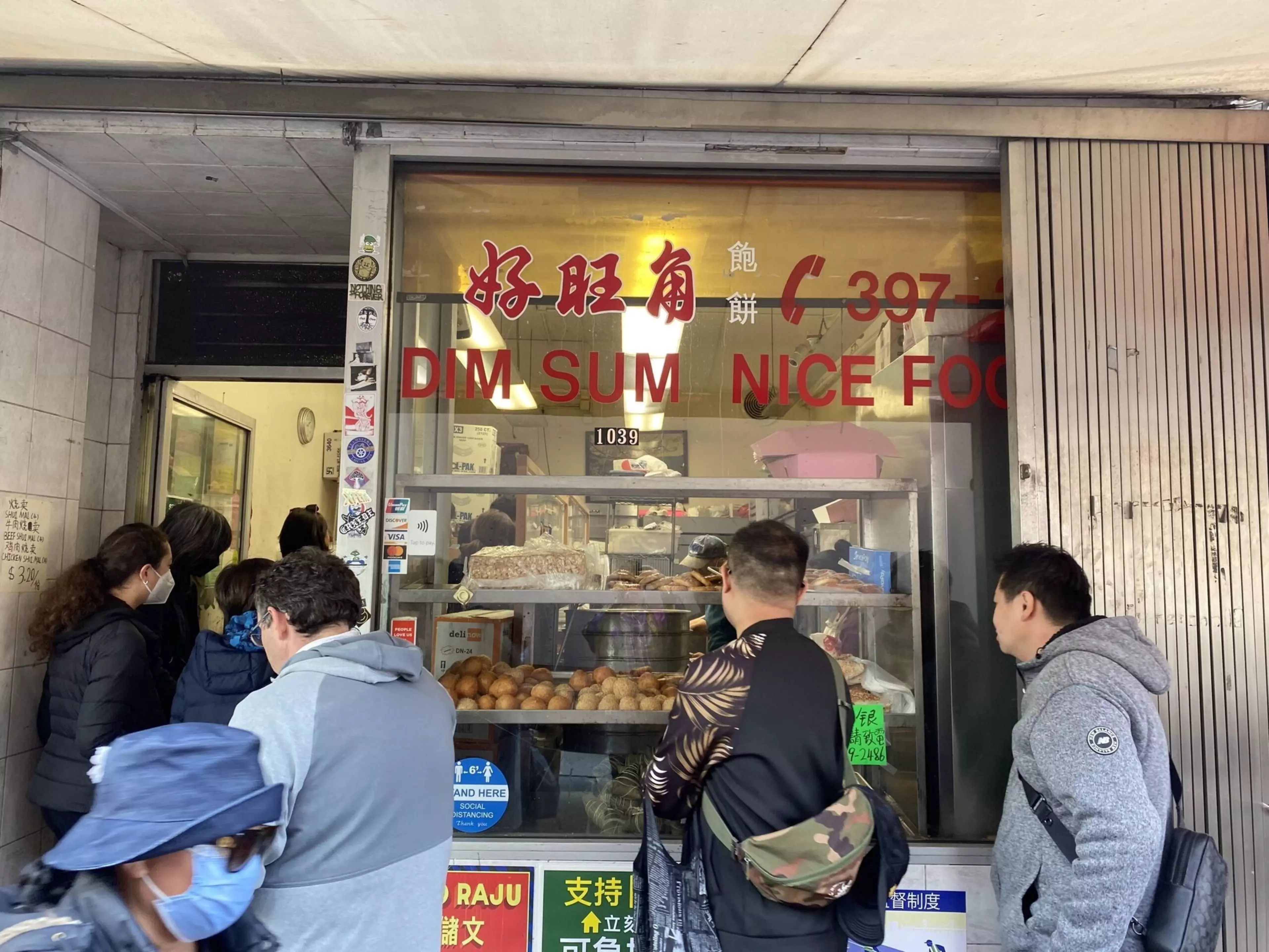 Patrons queue outside a Chinese bakery with platters of goods in the window.