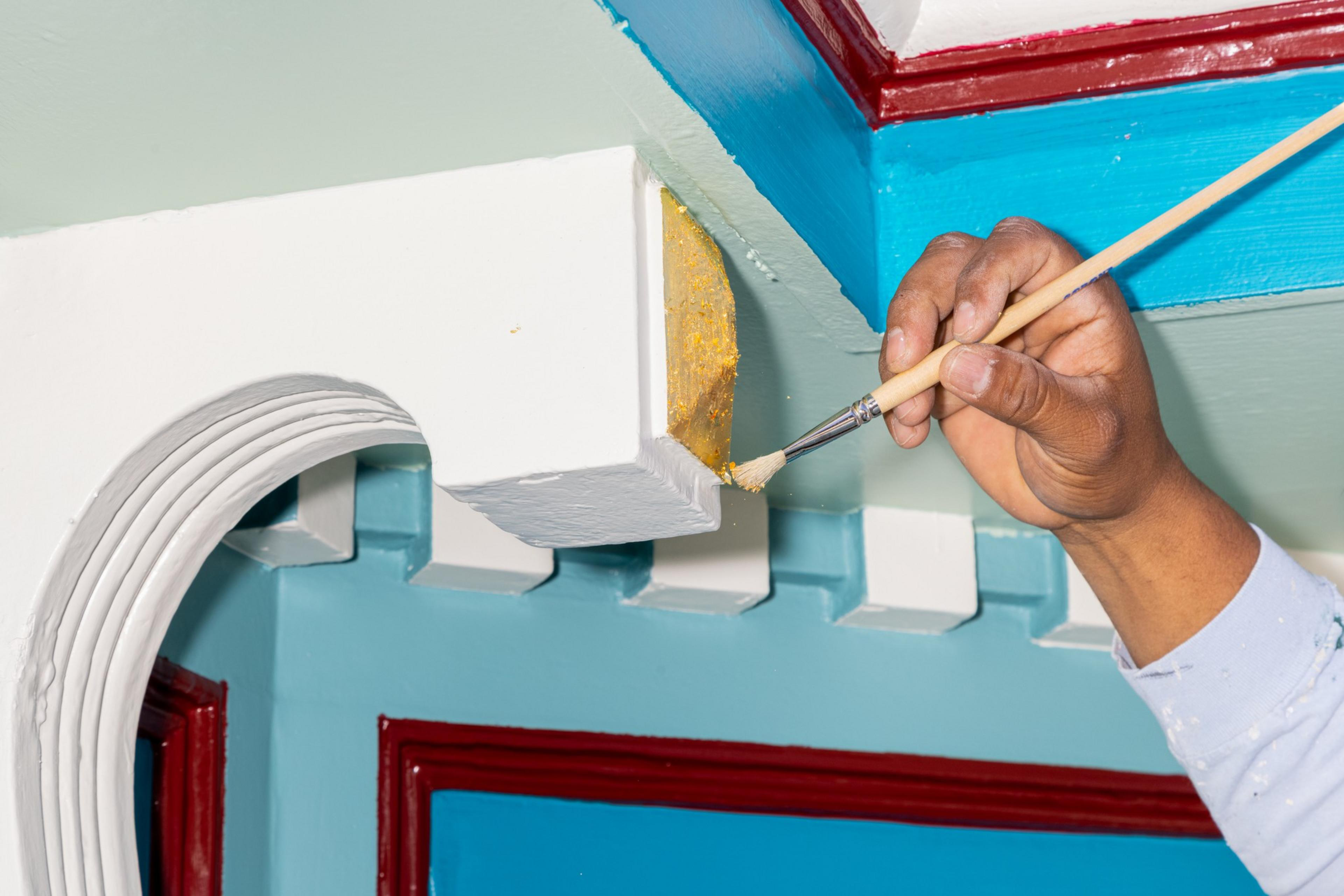 A hand is painting the edge of vibrant, multicolored architectural features.