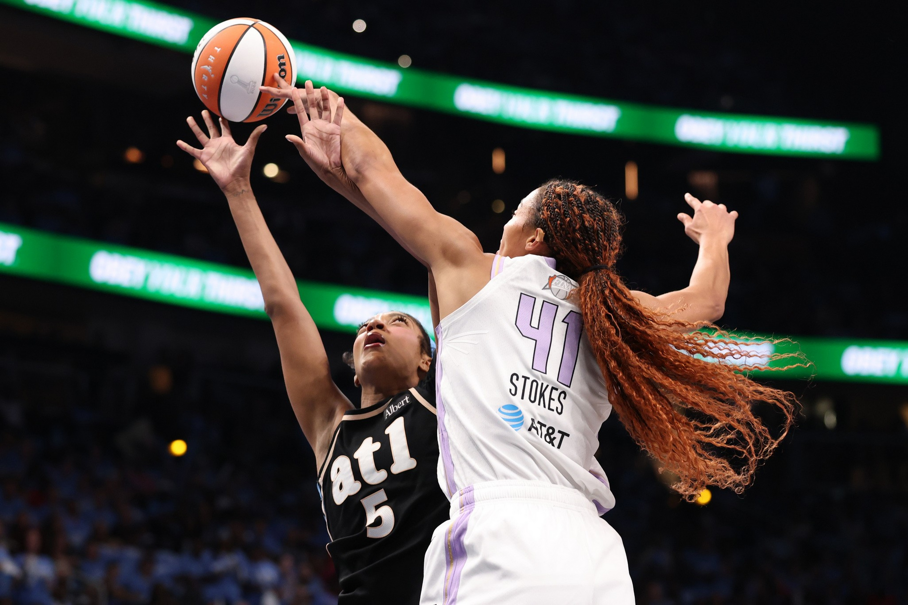 A basketball player in a white jersey with "41 Stokes" blocks a shot from a player in a black "atl" jersey numbered 5 during a game.