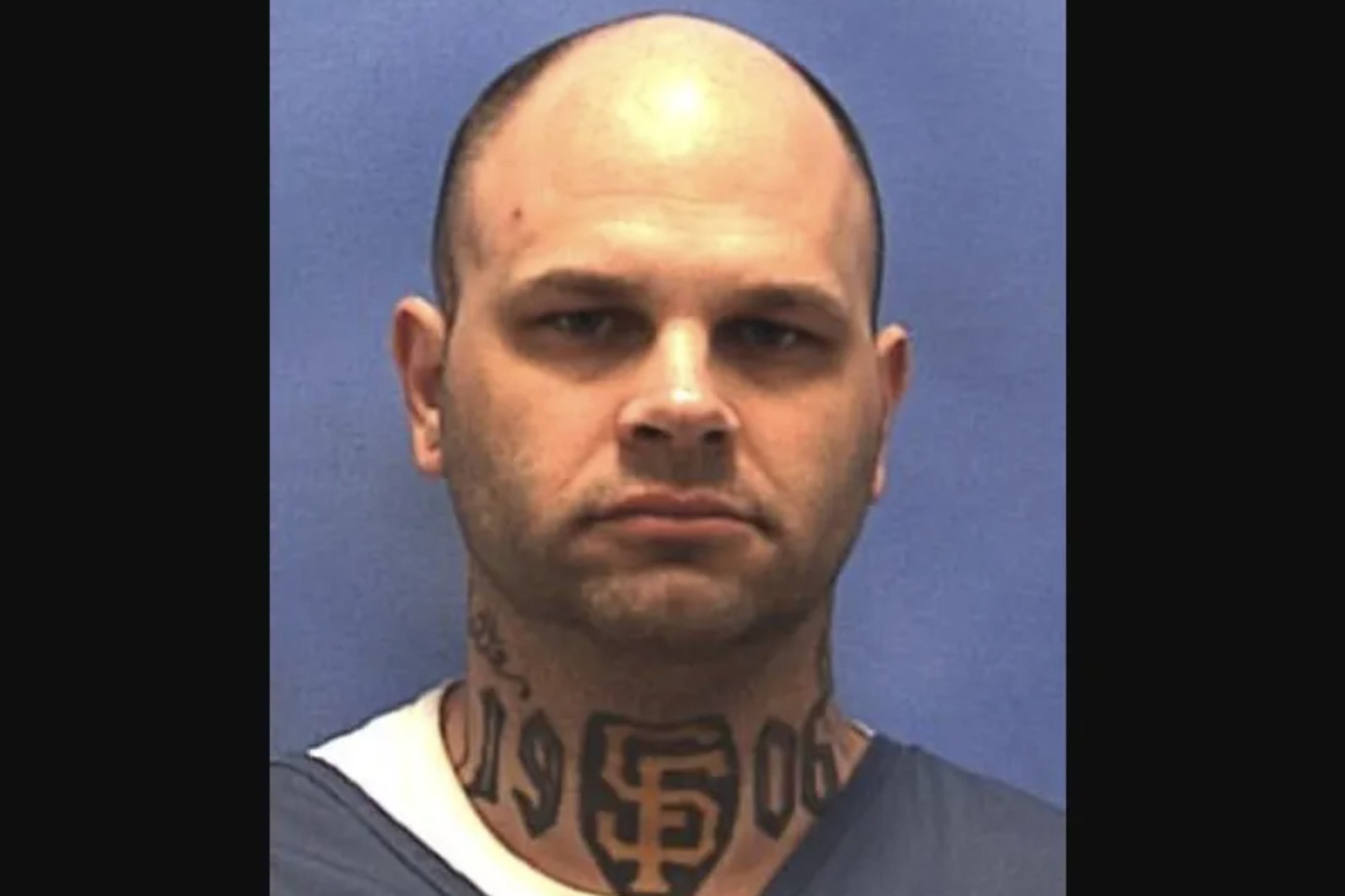 A bald man with a serious expression has a large neck tattoo featuring the letters "SF" and the numbers "19" and "06."