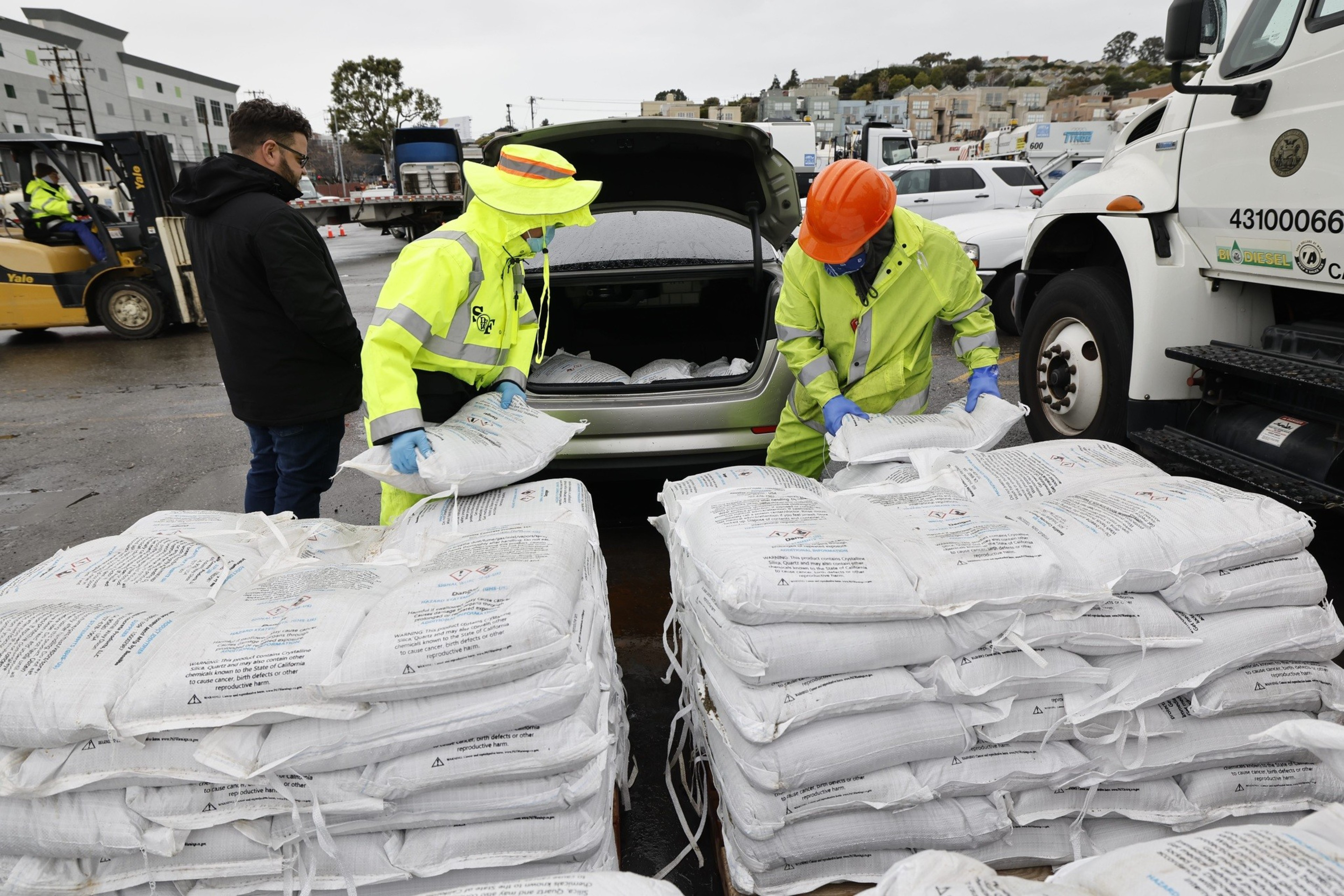 Men wearing neon uniforms help to pack levees into a car during an intense storm in January 2023.