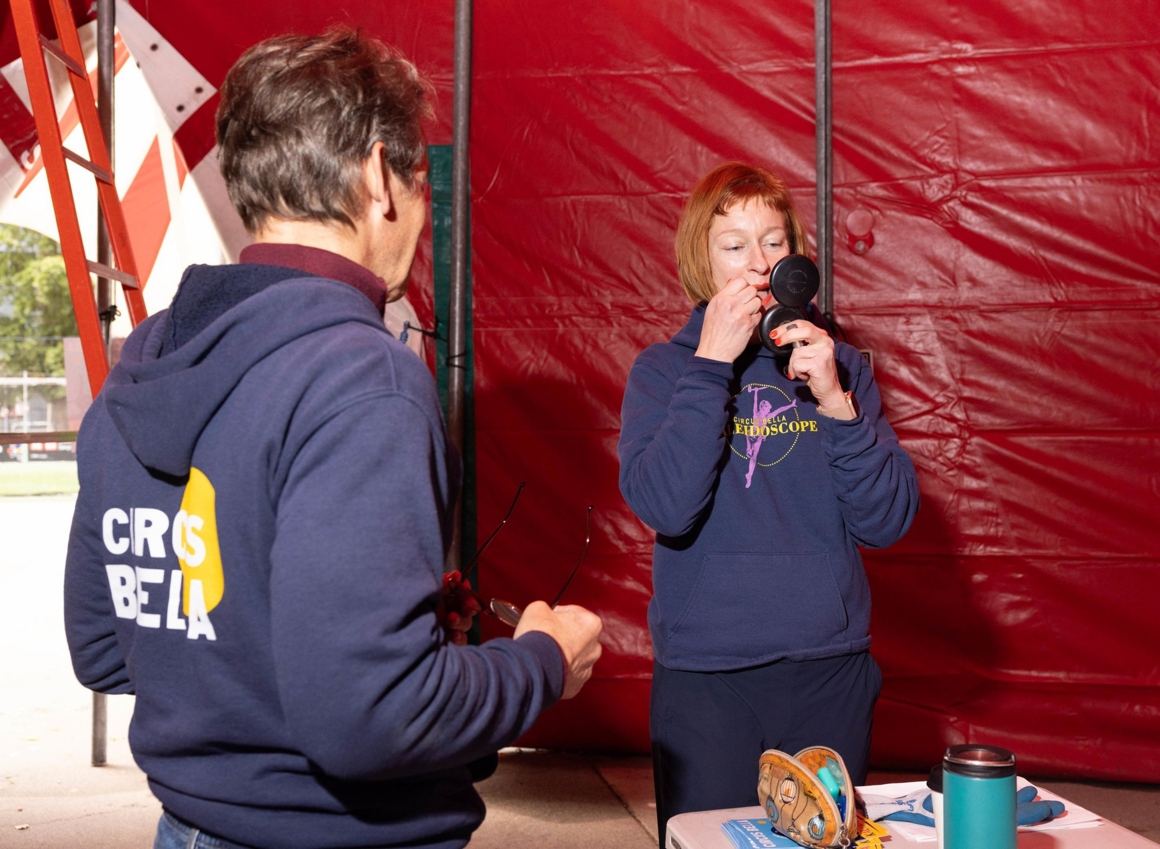 Two people talk as another person puts on lip stick.