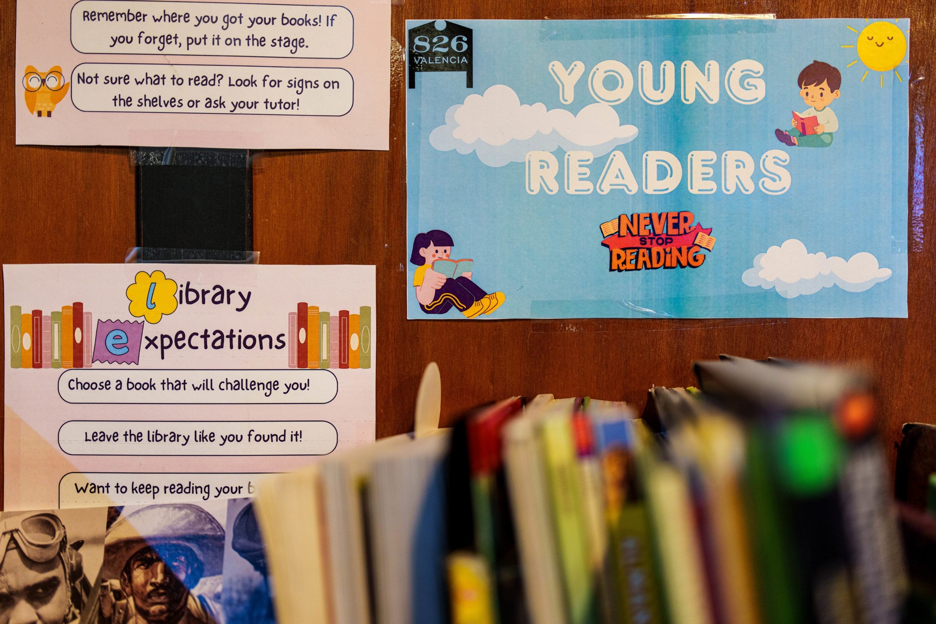 Signs on a wooden shelf include “Library Expectations” and “Young Readers,” accompanied by cartoon kids reading and library guidelines displayed.