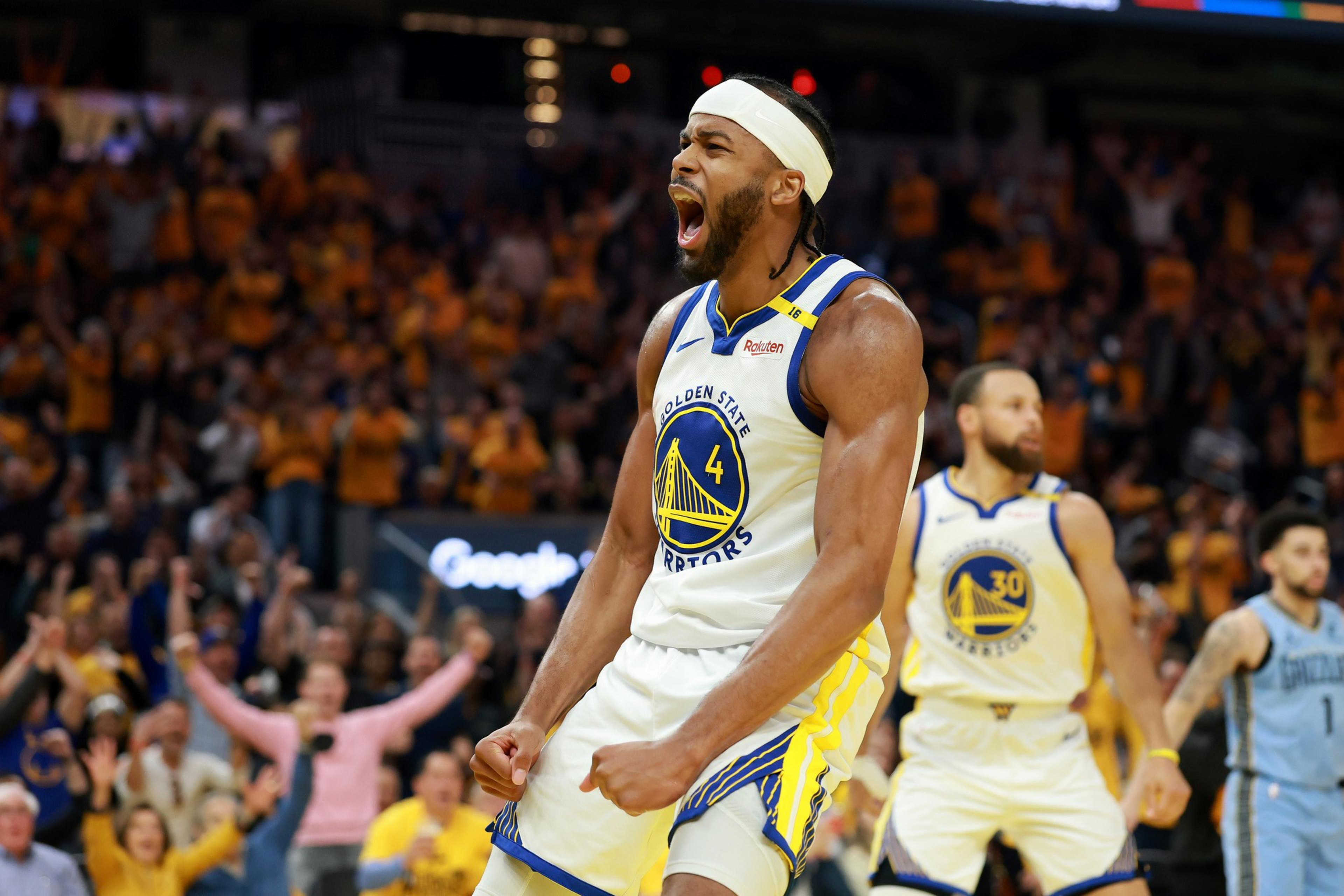 A basketball player in a Golden State Warriors jersey, number 4, is passionately shouting on the court. The crowd in the arena is cheering enthusiastically behind him.
