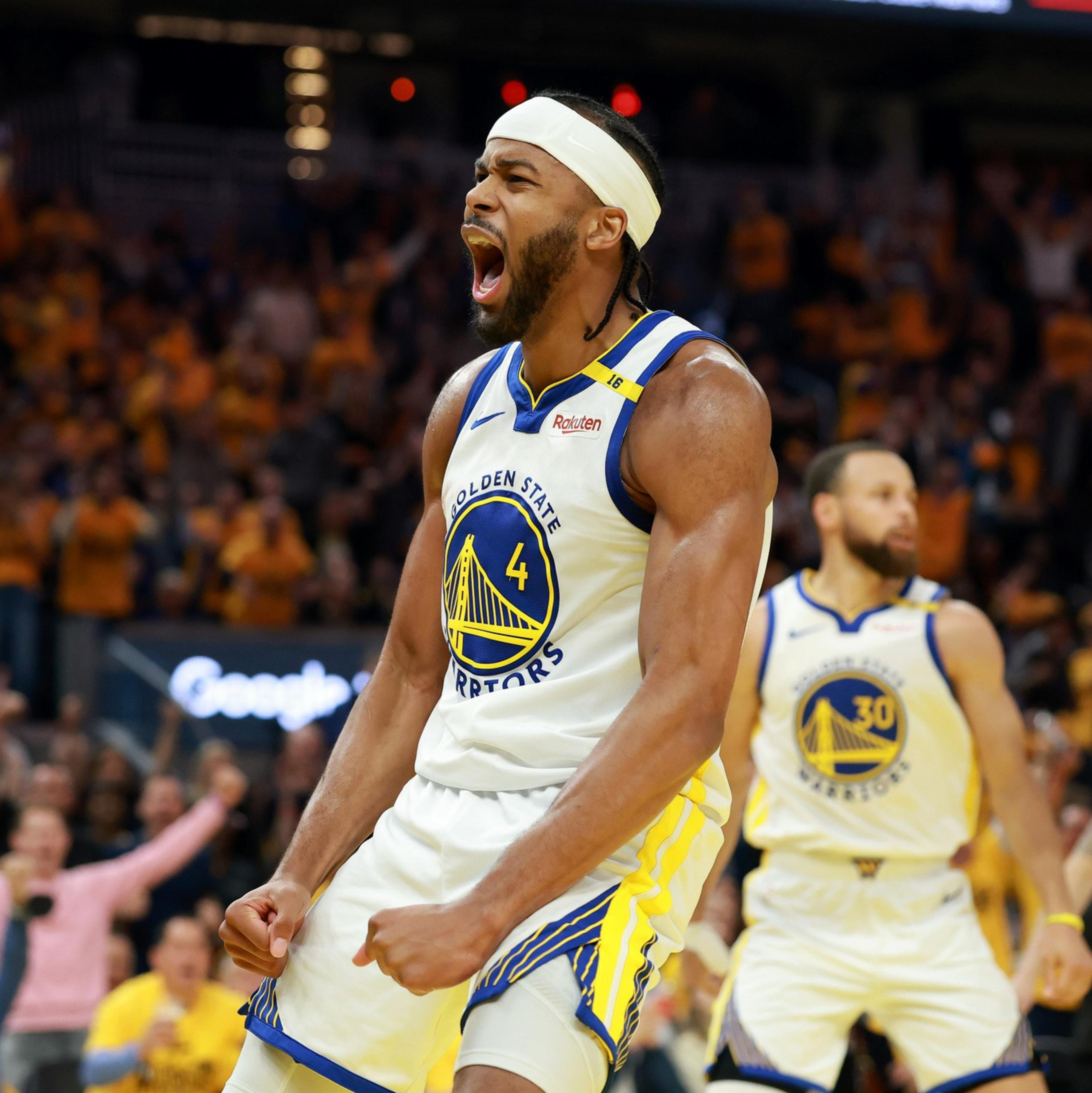 A basketball player in a Golden State Warriors jersey, number 4, is passionately shouting on the court. The crowd in the arena is cheering enthusiastically behind him.