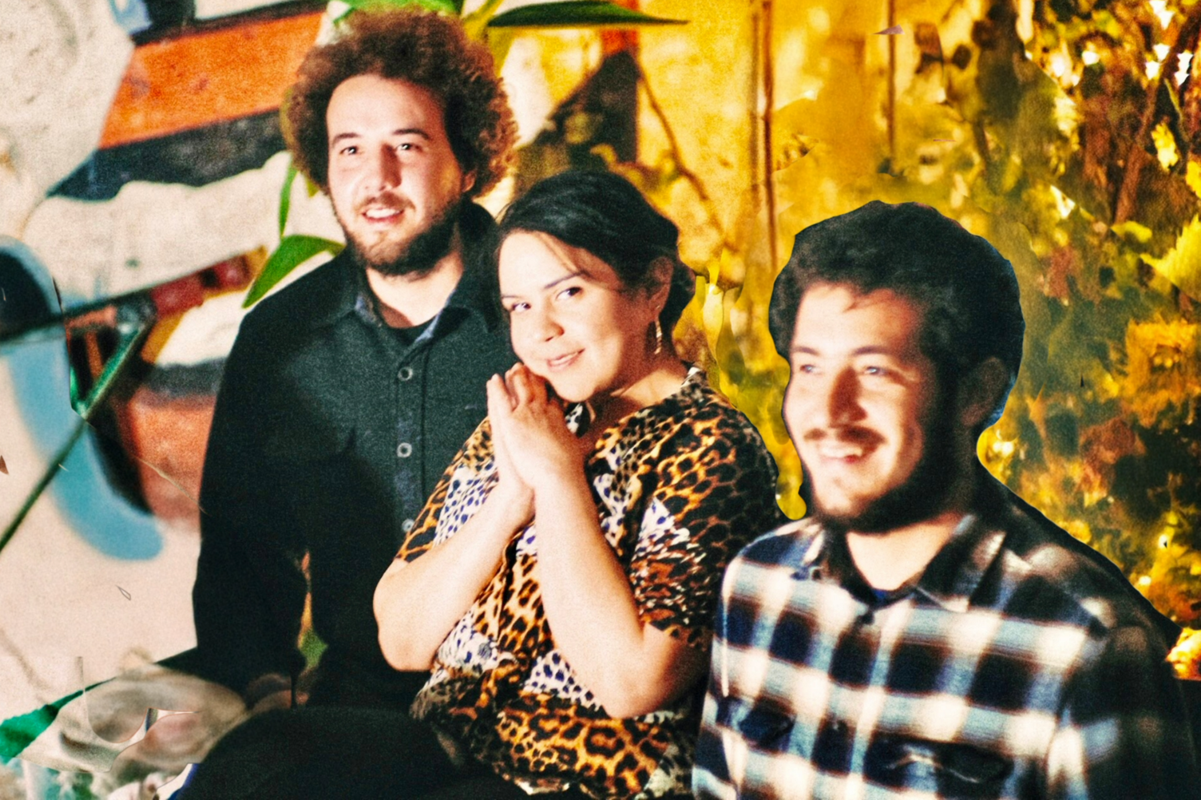 Three people sit close together indoors, two men with facial hair and a woman in a leopard-print shirt smiling warmly against a leafy, warmly lit backdrop.