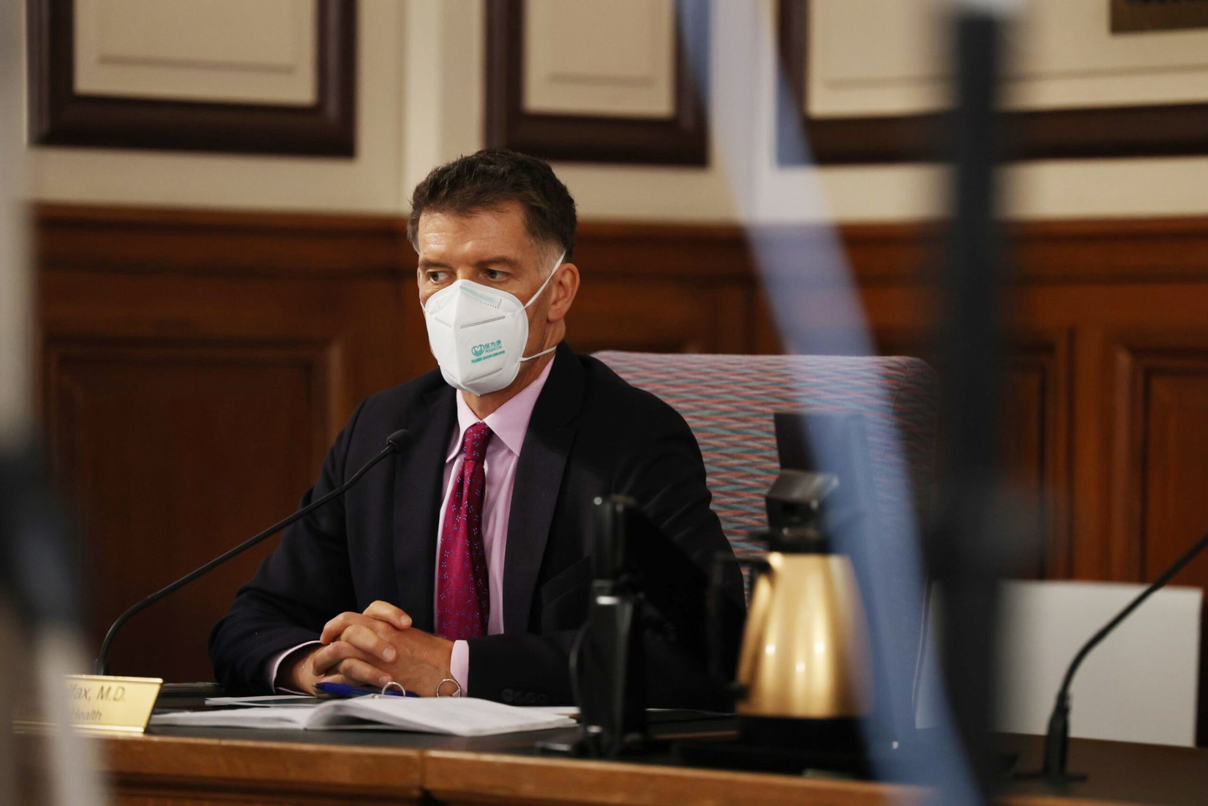 A man sits at a desk with his hands folded.