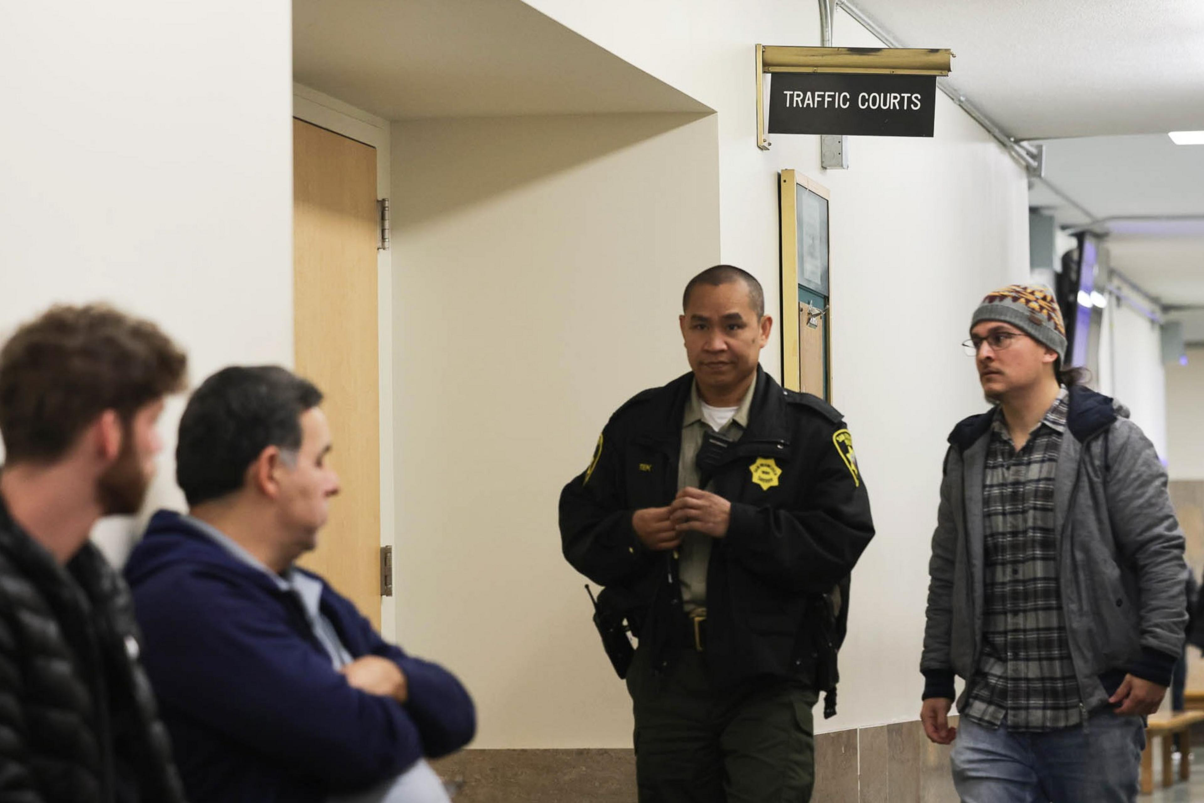 Three people look at a Sheriff's Department deputy standing outside a doorway.