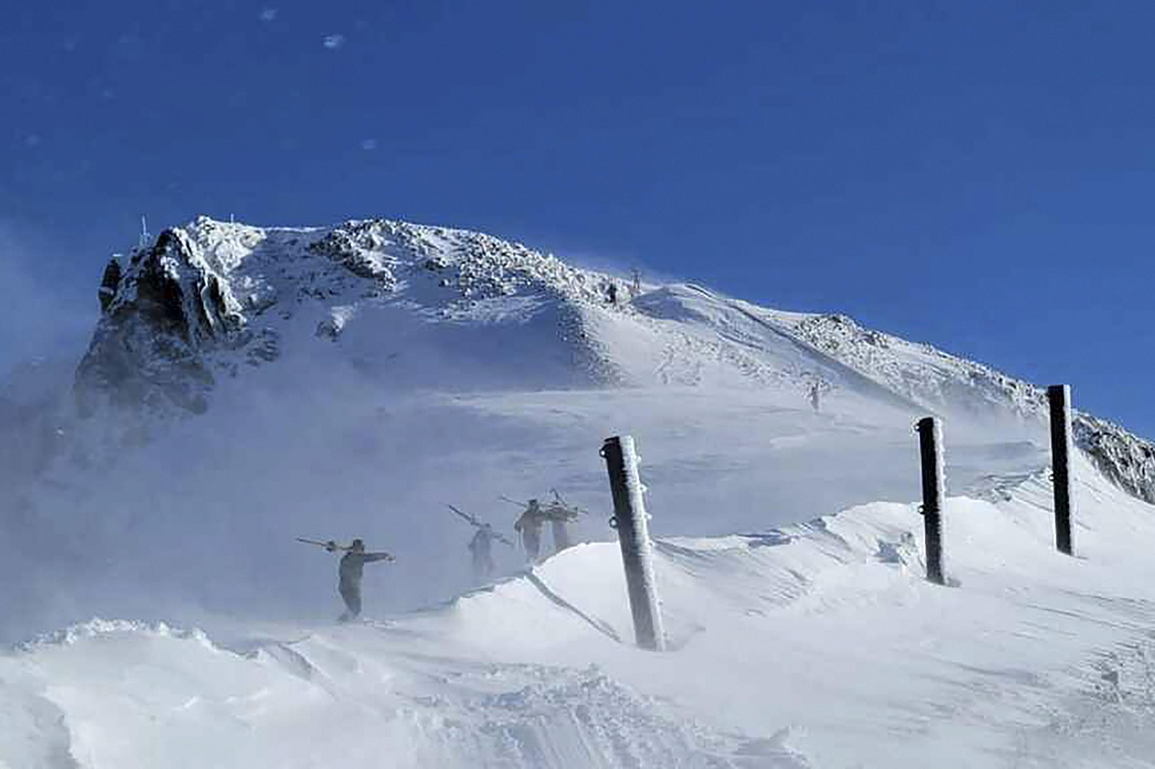 Skiers hike through the snow in front of a snowcapped mountain peak