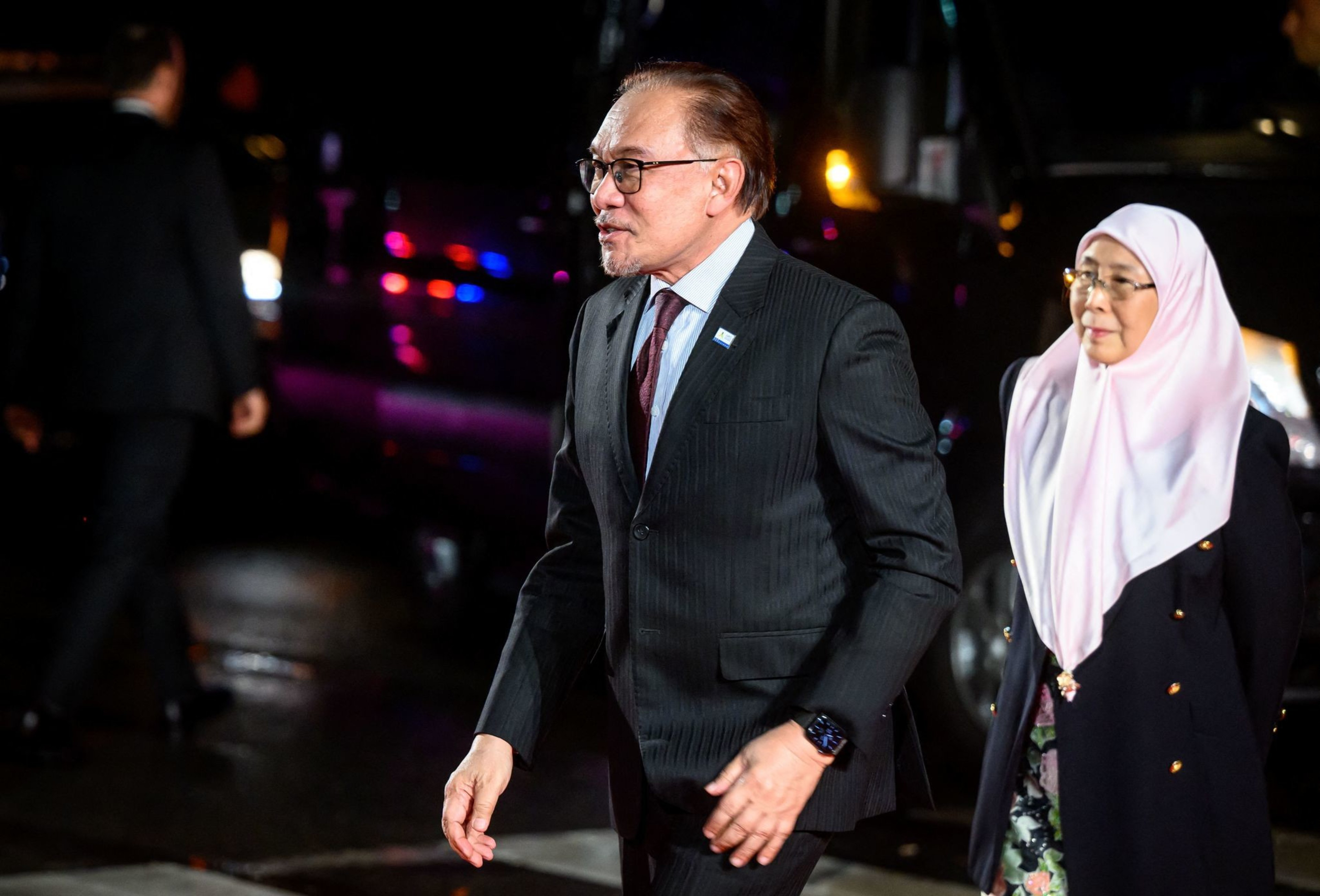 Malaysia's Primer Minister Anwar Ibrahim arrives at an event with a woman wearing a headscarf walk behind walks him.