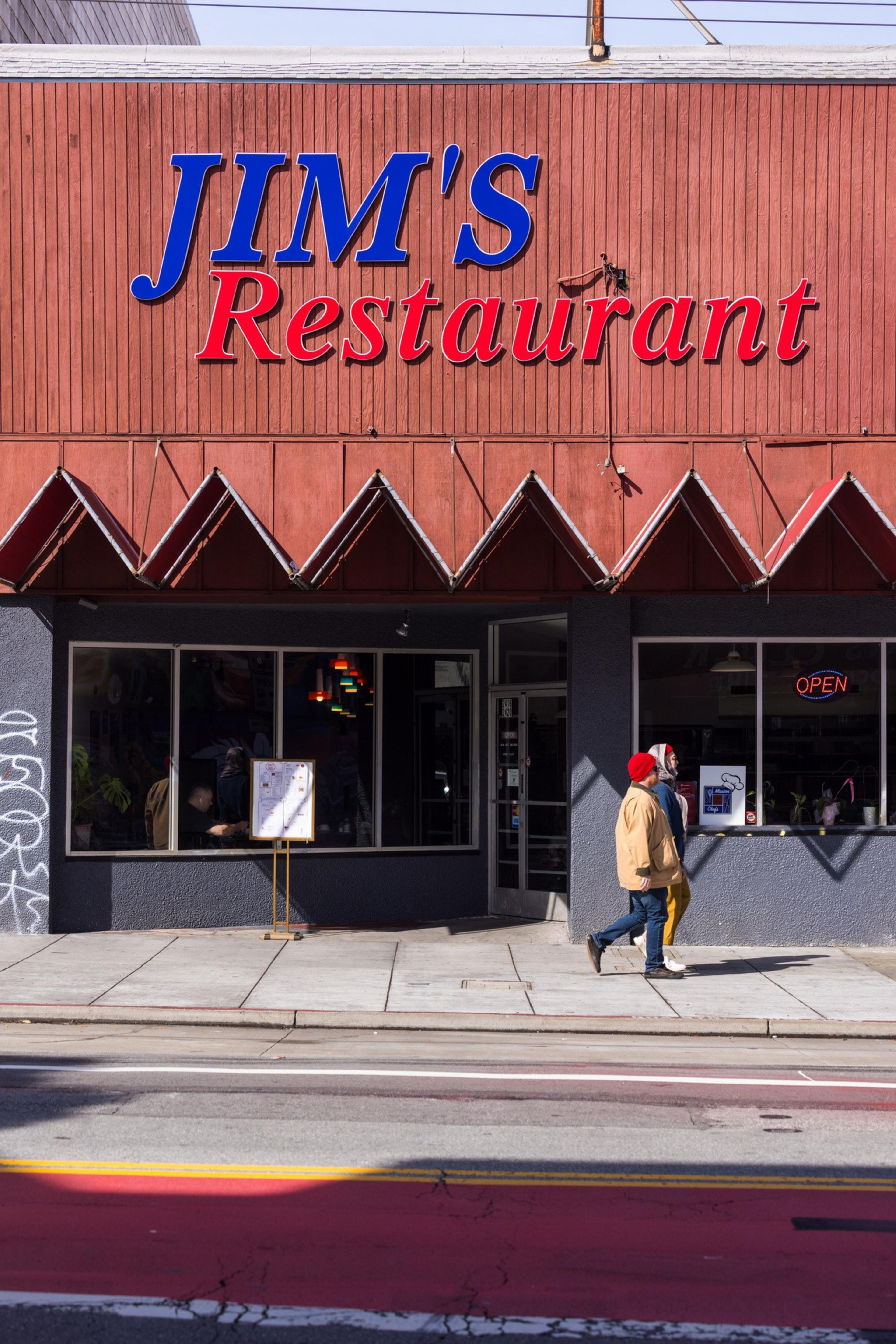 A red and brown facade reads &quot;Jim's Restaurant&quot; with two people walking by on the sidewalk. An &quot;open&quot; sign is visible in the window.