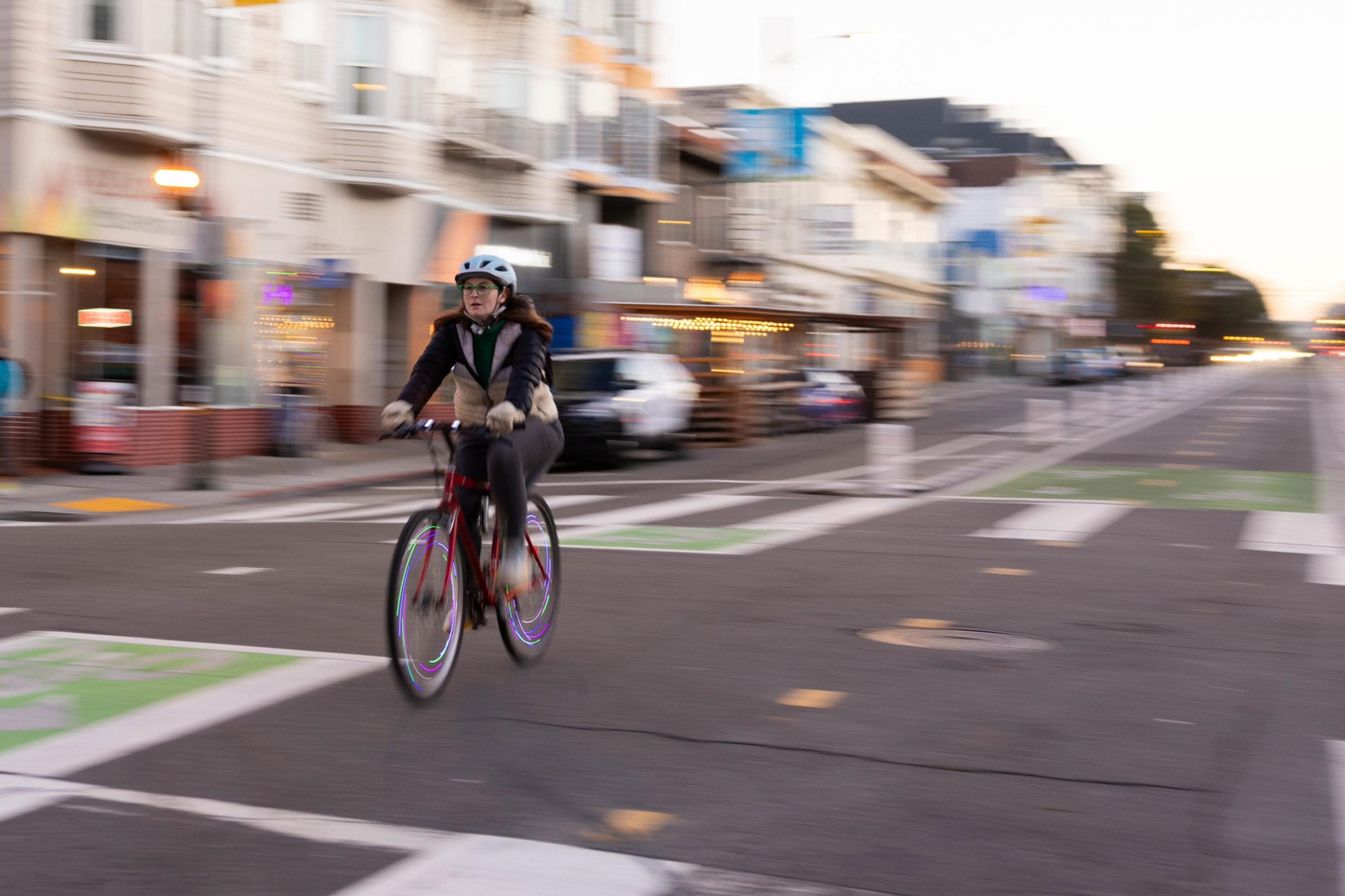 A person cycling on a city street at dusk, motion blur emphasizes their movement.
