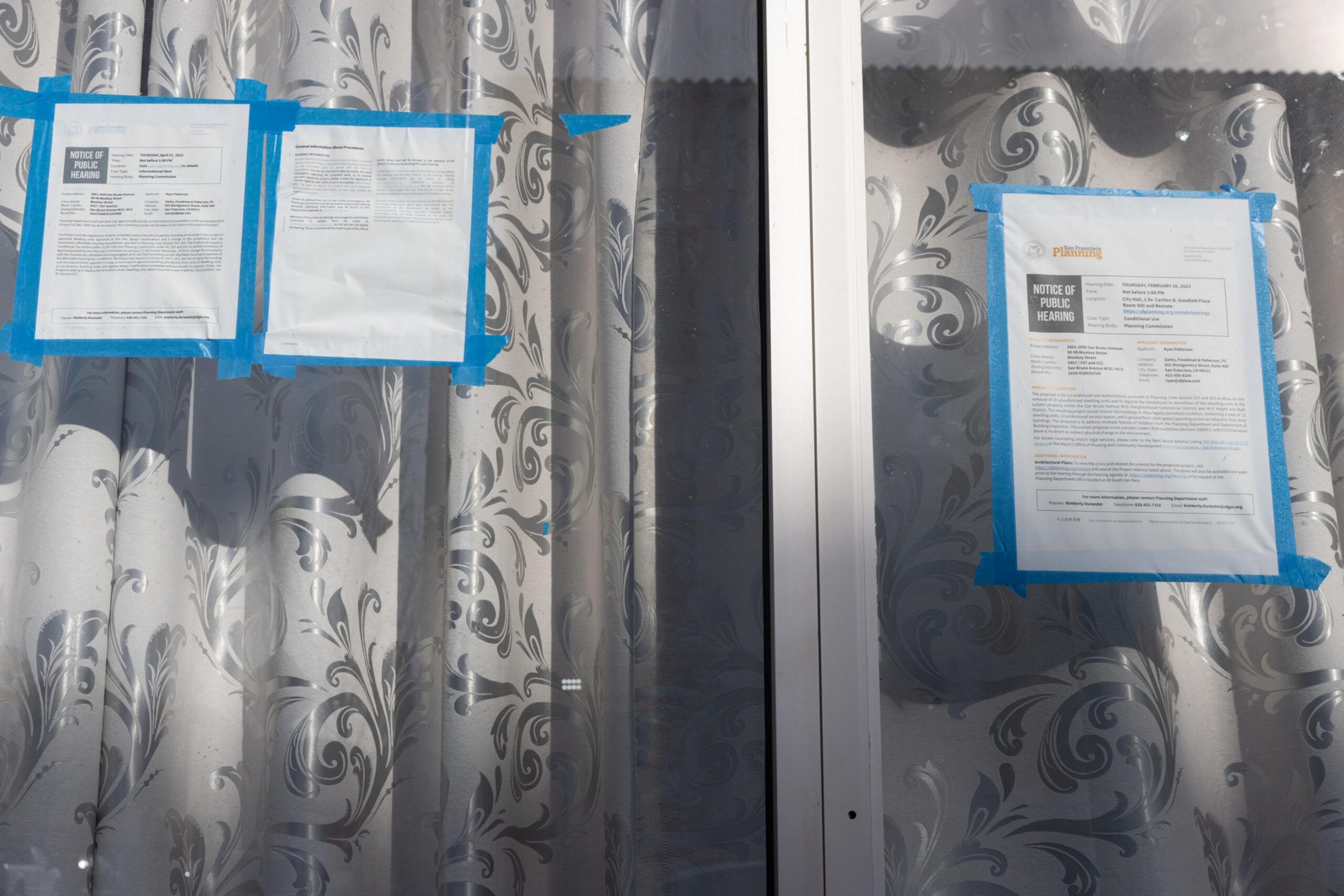 Three printed notices taped with blue tape are posted on glass doors covered by patterned curtains.