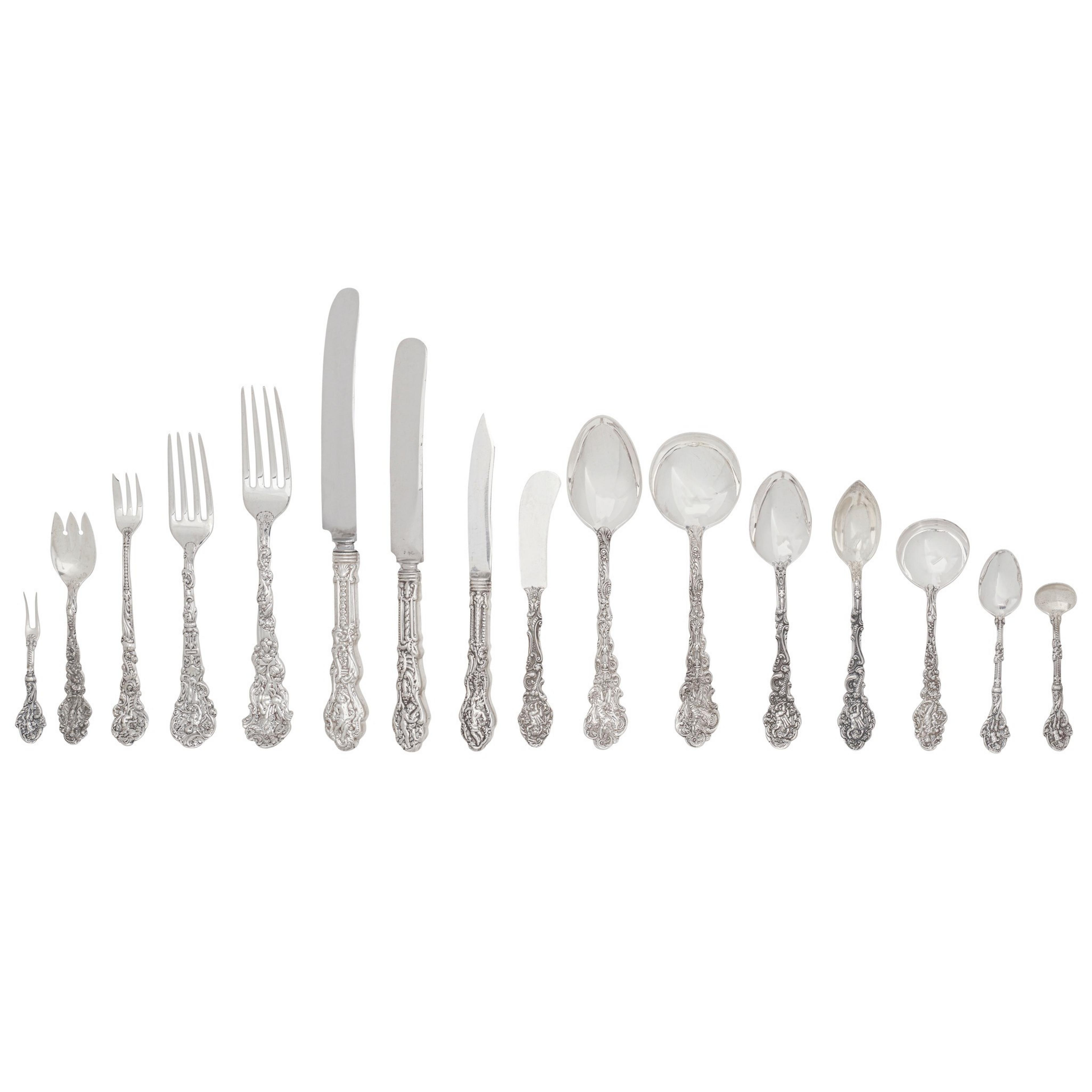 The image shows an elegant set of silver cutlery arranged in a line, featuring forks, knives, and various spoons with intricate ornate handles.