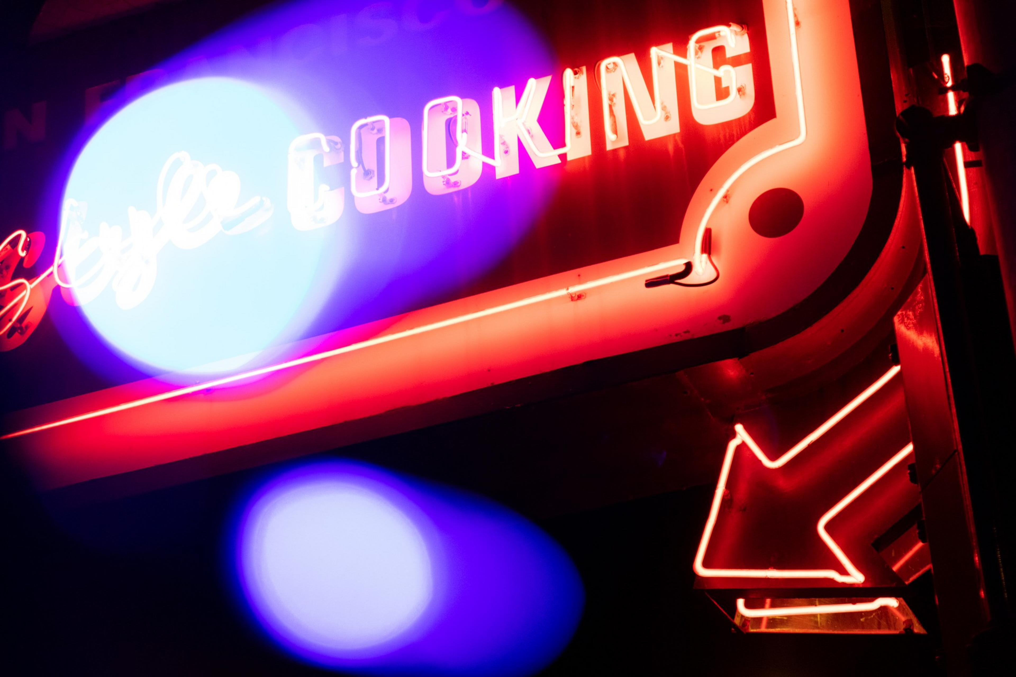 A red neon sign a night with the words &quot;COOKING&quot; and an arrow pointing downwards