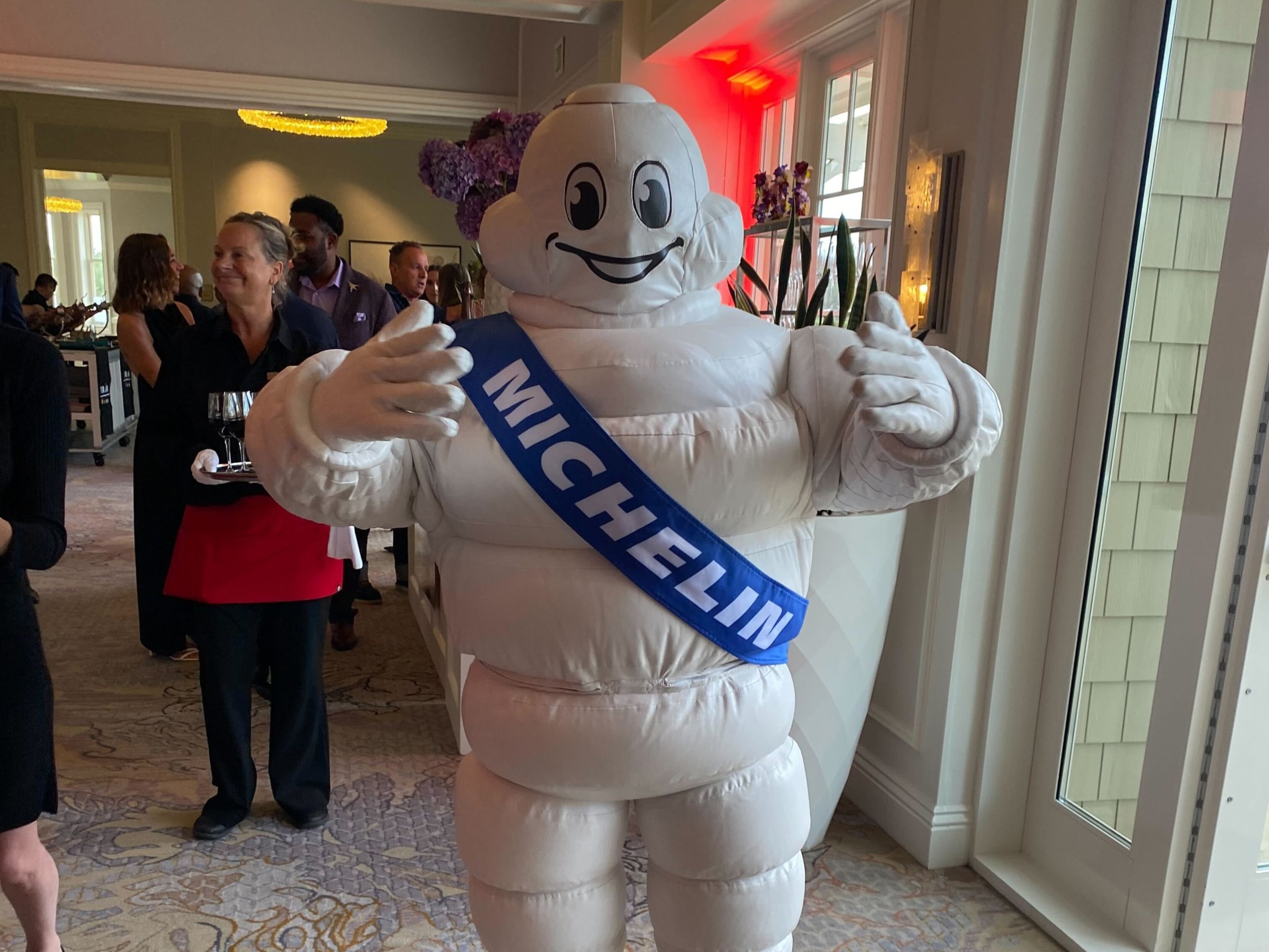 A person in a Michelin tire man costumer poses in a hallway.