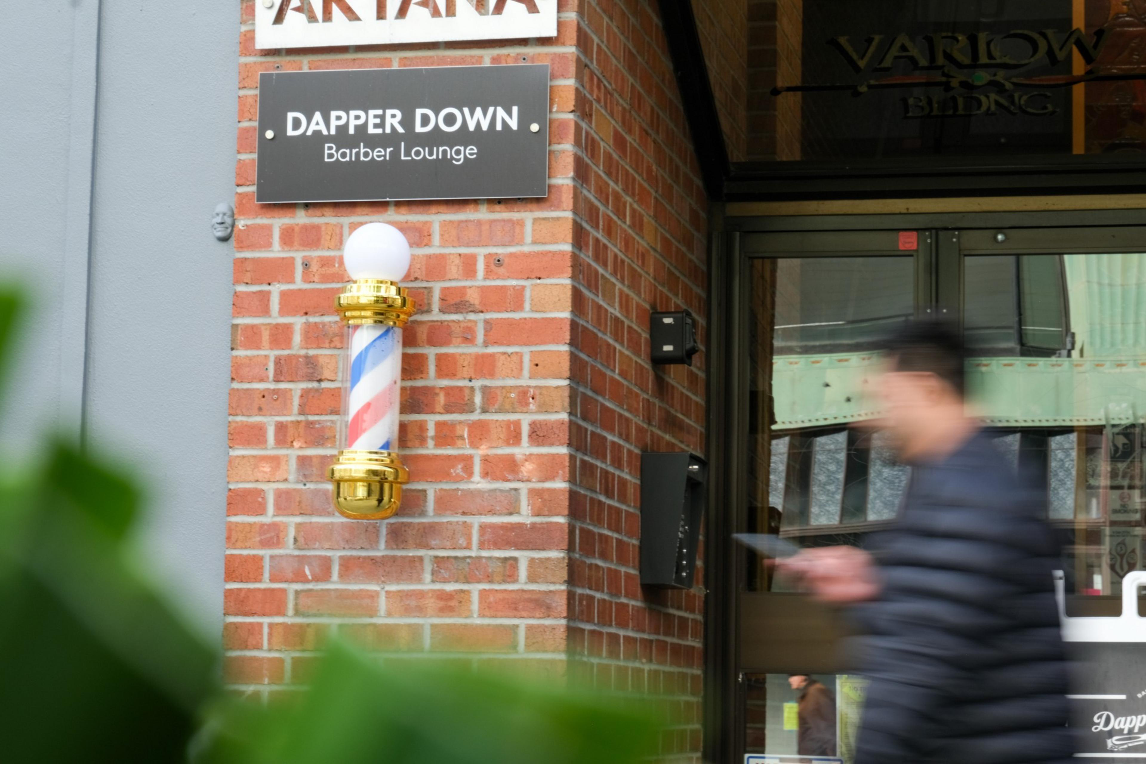 A rotating barber's pole with a blurred person walking by outside a barber lounge.