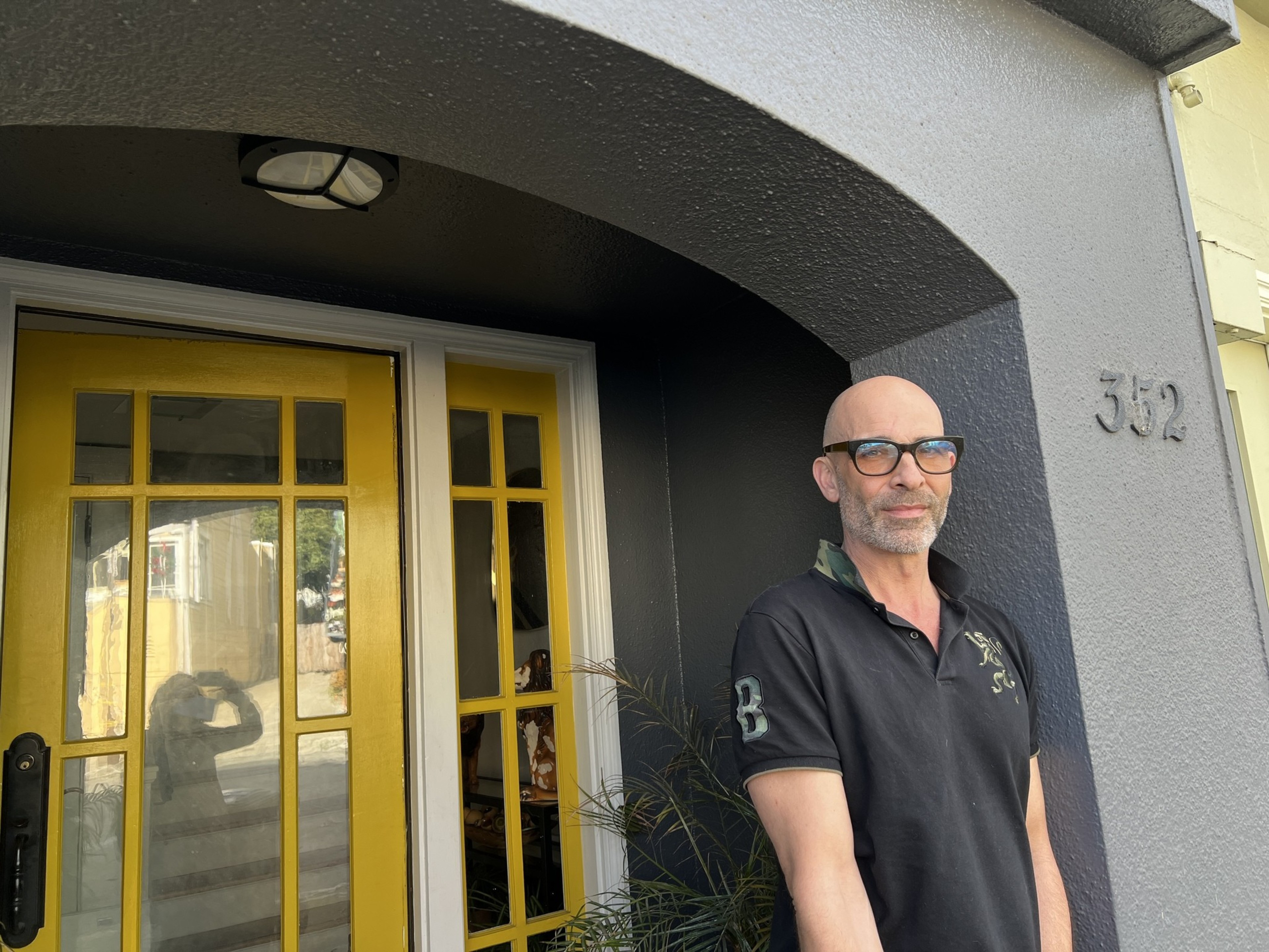 A man stands in a black shirt in front of a yellow door.