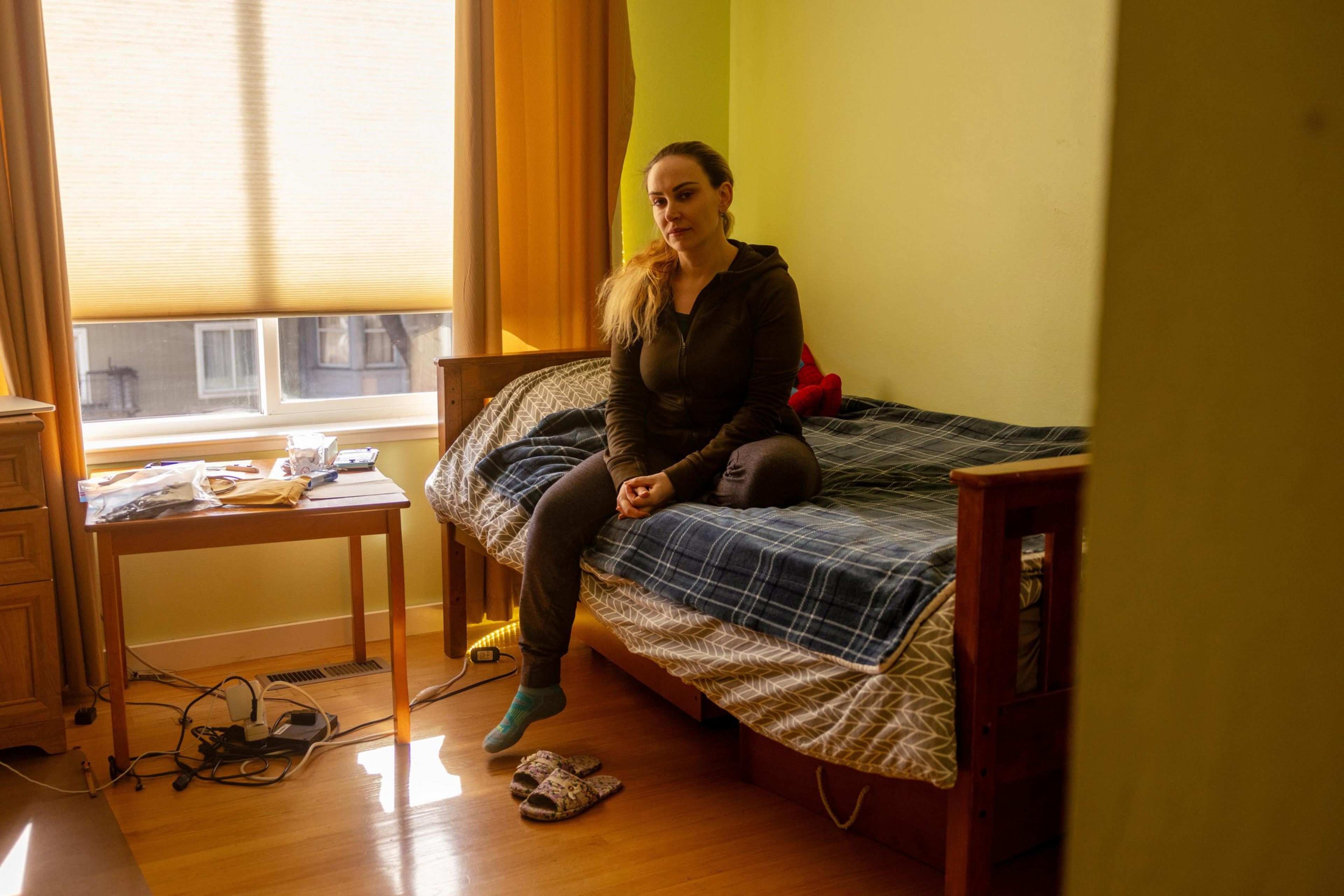A woman sits on a bed for a photo portrait.