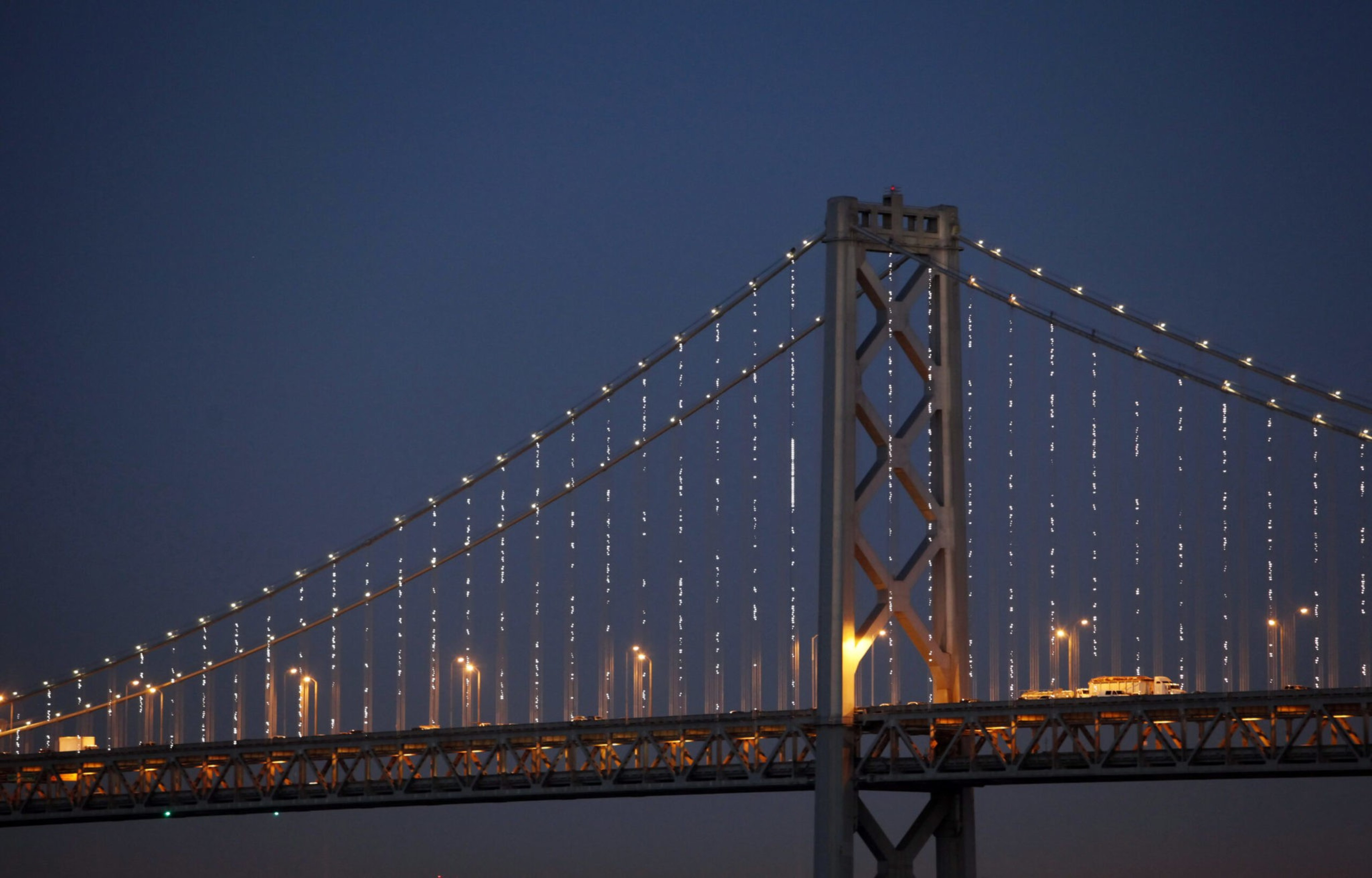A light show illuminating cables on a suspension bridge shine at night.