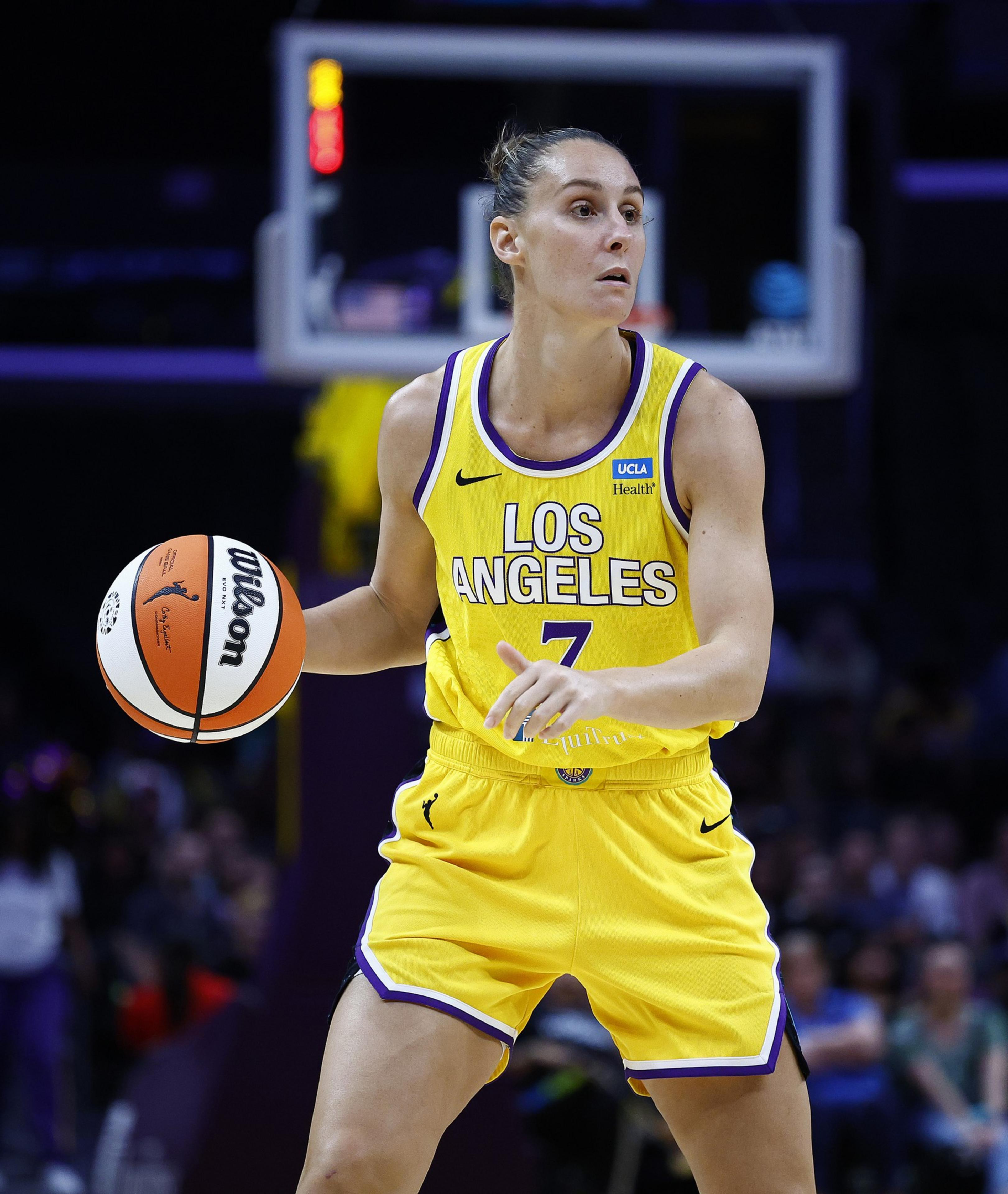 A basketball player in a yellow &quot;Los Angeles&quot; jersey, number 7, is dribbling a Wilson ball on a court, focused on the game.