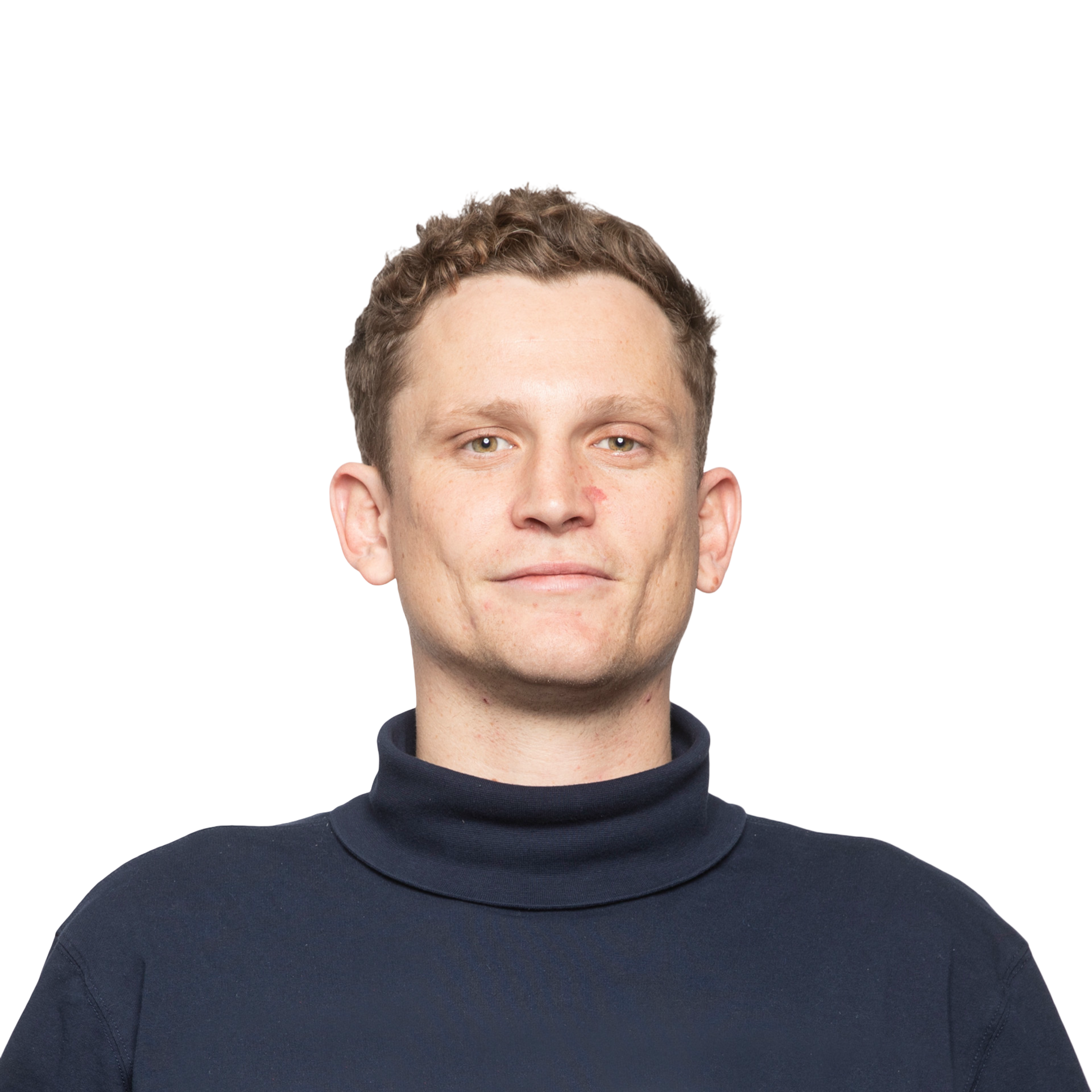 A man with short curly brown hair wears a navy blue turtleneck and looks directly at the camera with a neutral expression.
