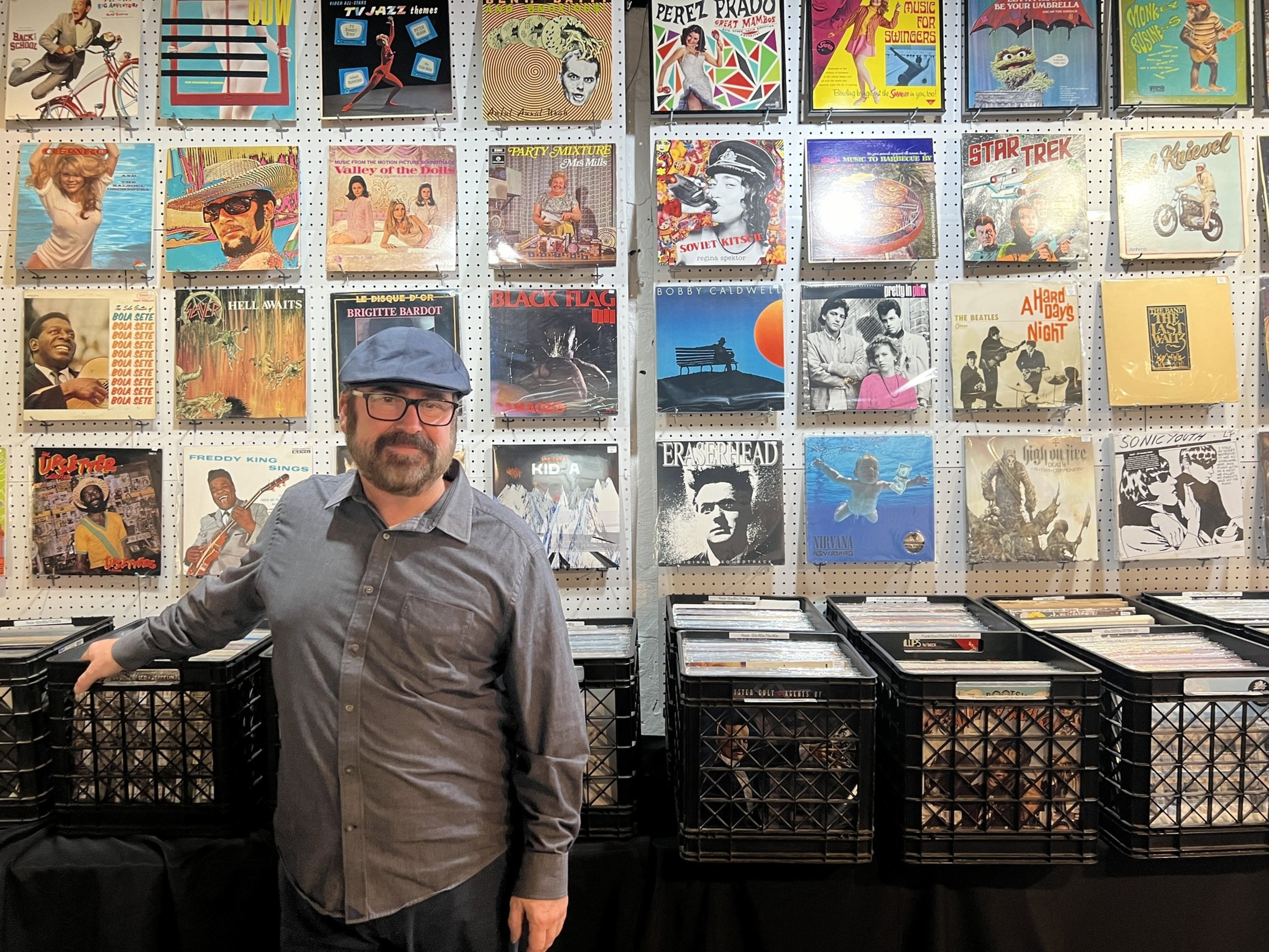 A man stands in front of cases of records with records behind him on the wall.