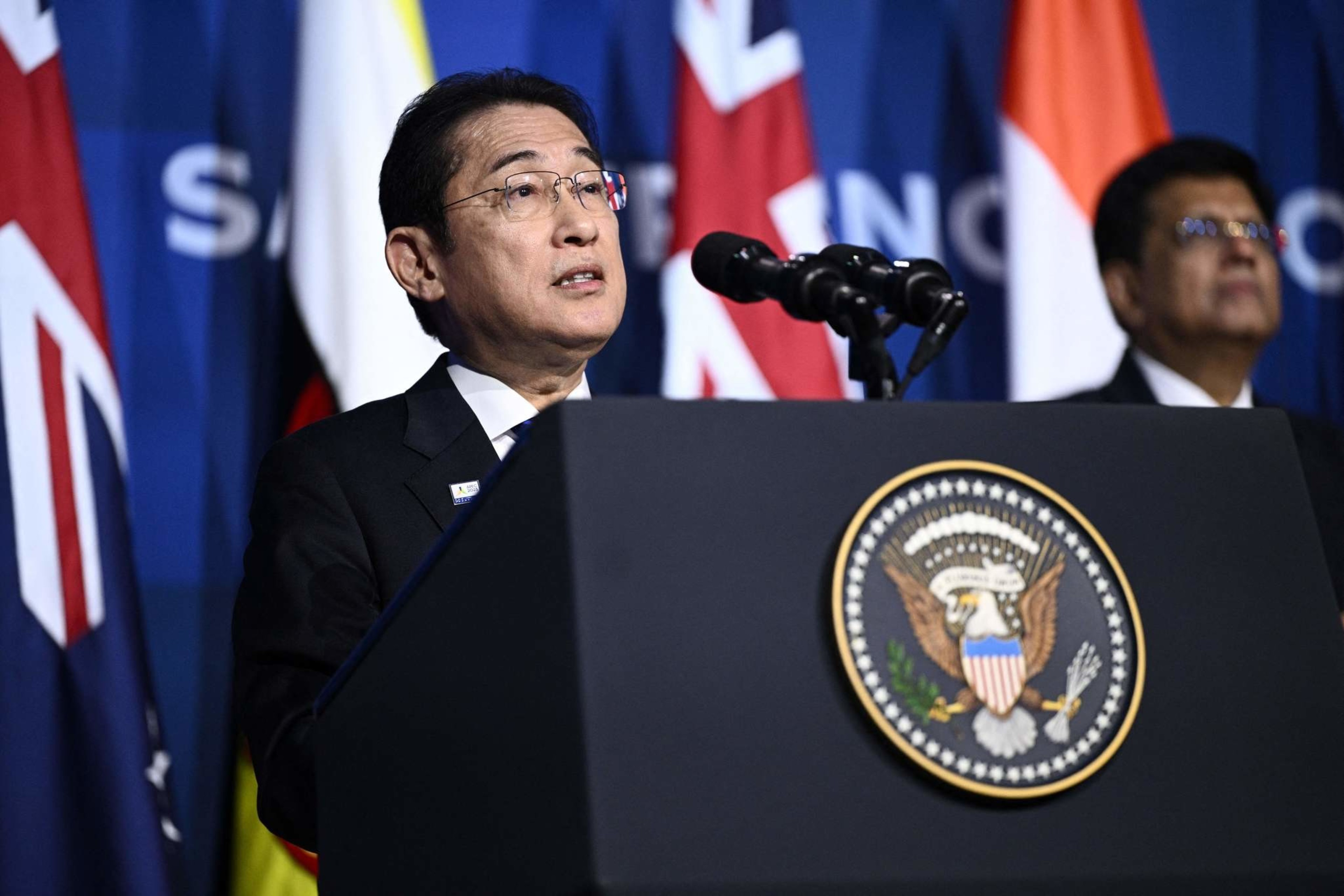 Japan's Prime Minister Fumio Kishida (L) delivers remarks on stage.