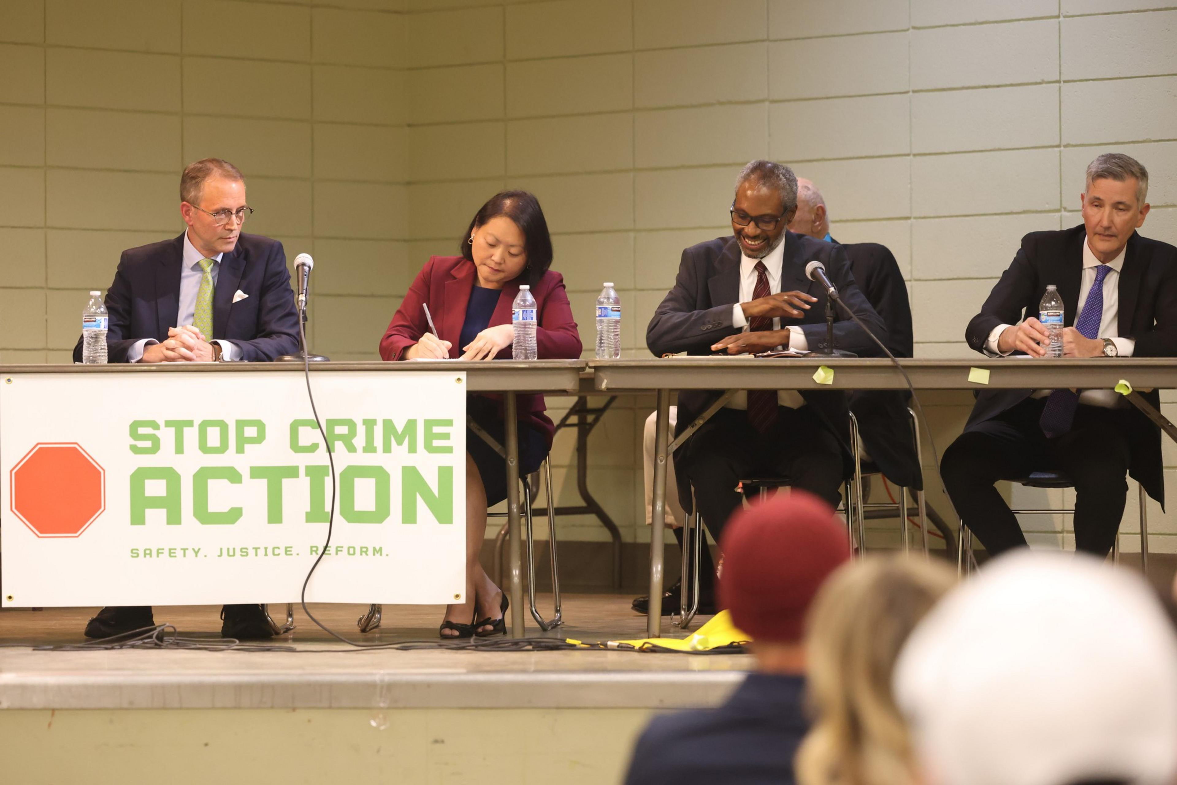 Four judge candidates sit at a table on a stage.