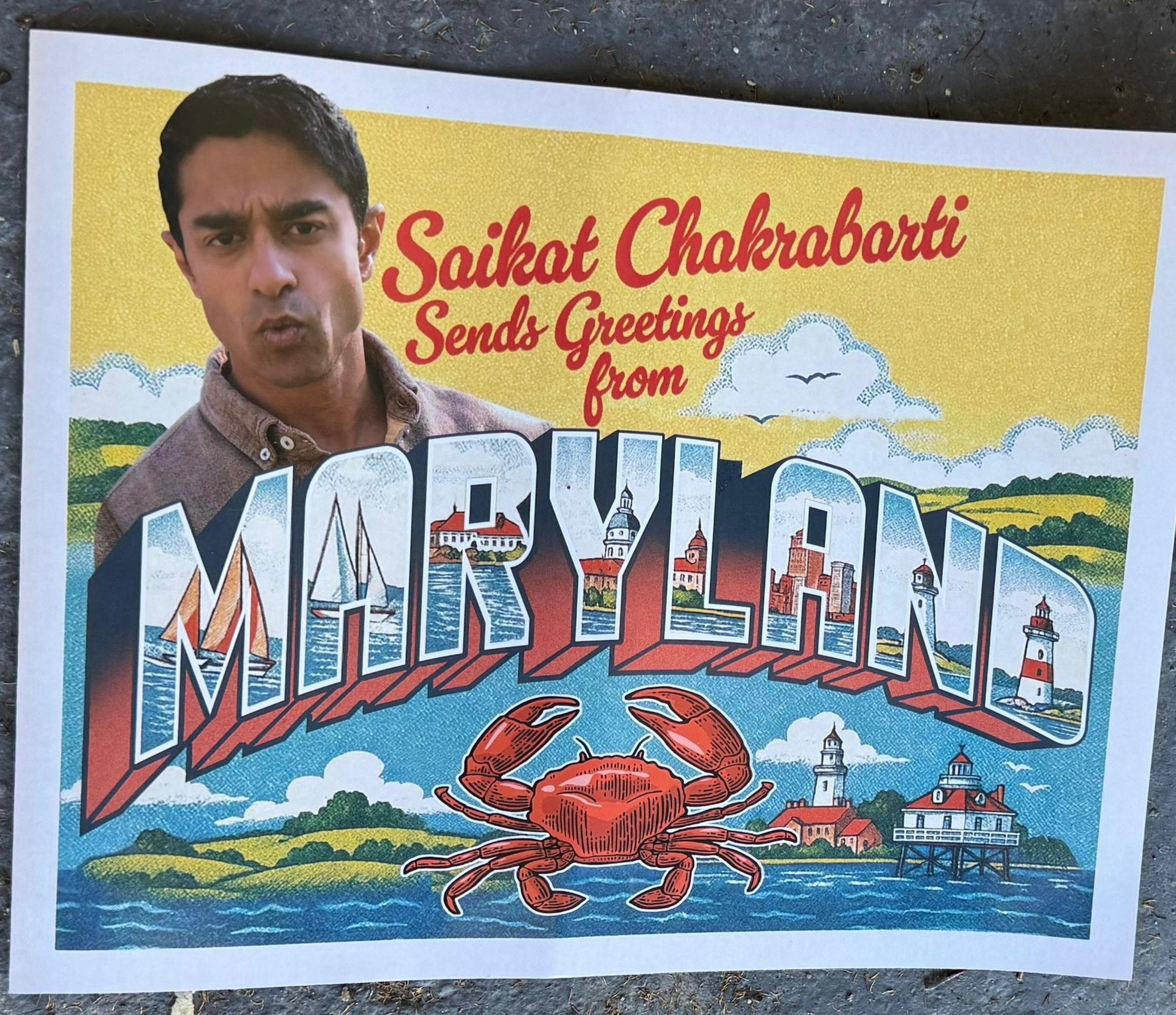 Saikat Chakrabarti poses with an illustrated postcard reading “Sends Greetings from MARYLAND,” featuring a red crab, lighthouses, water, and landscapes.