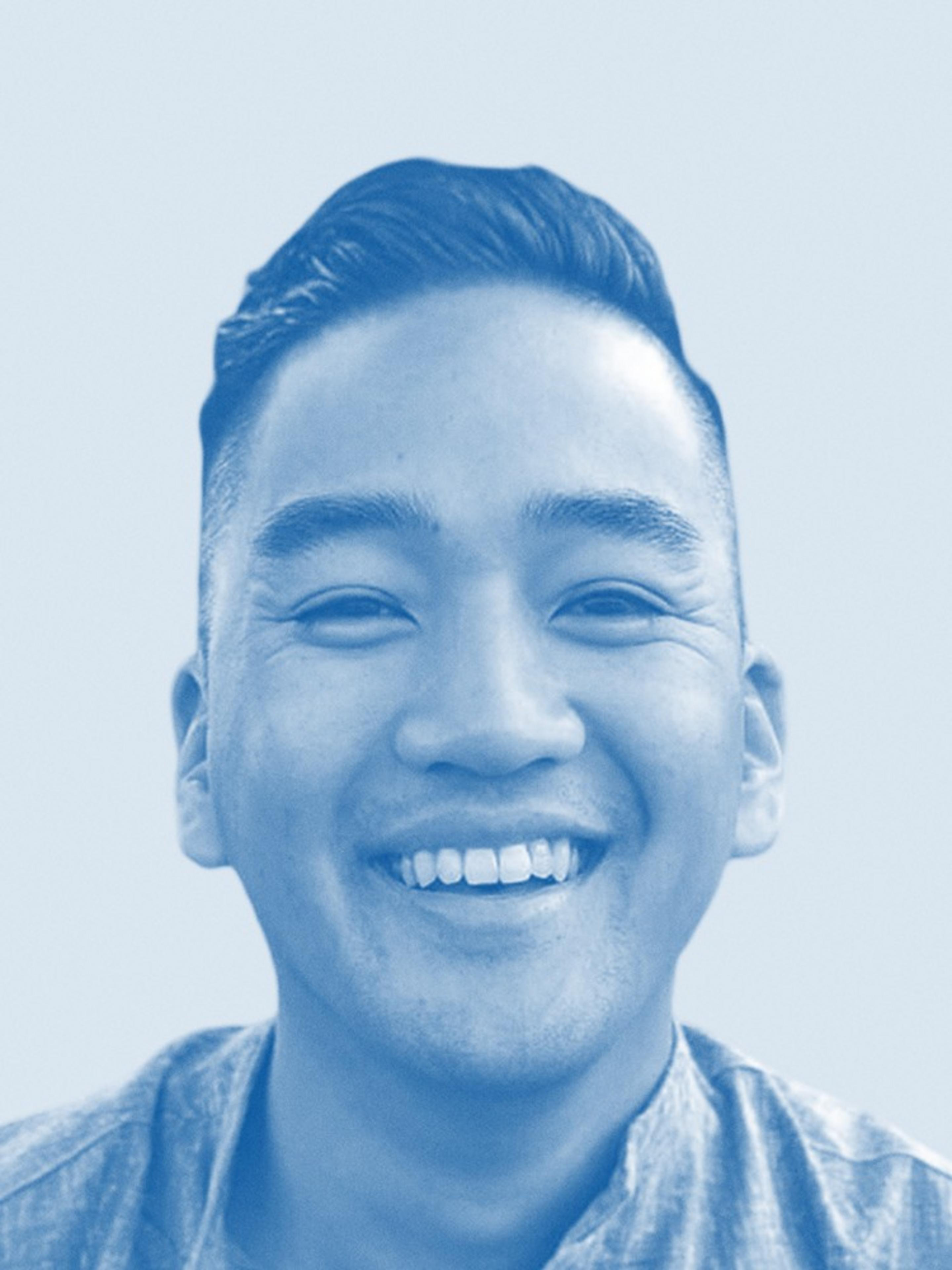 The image shows a smiling person with short, neatly styled hair, wearing a shirt. The photo has a blue tint, giving it a monochromatic look.