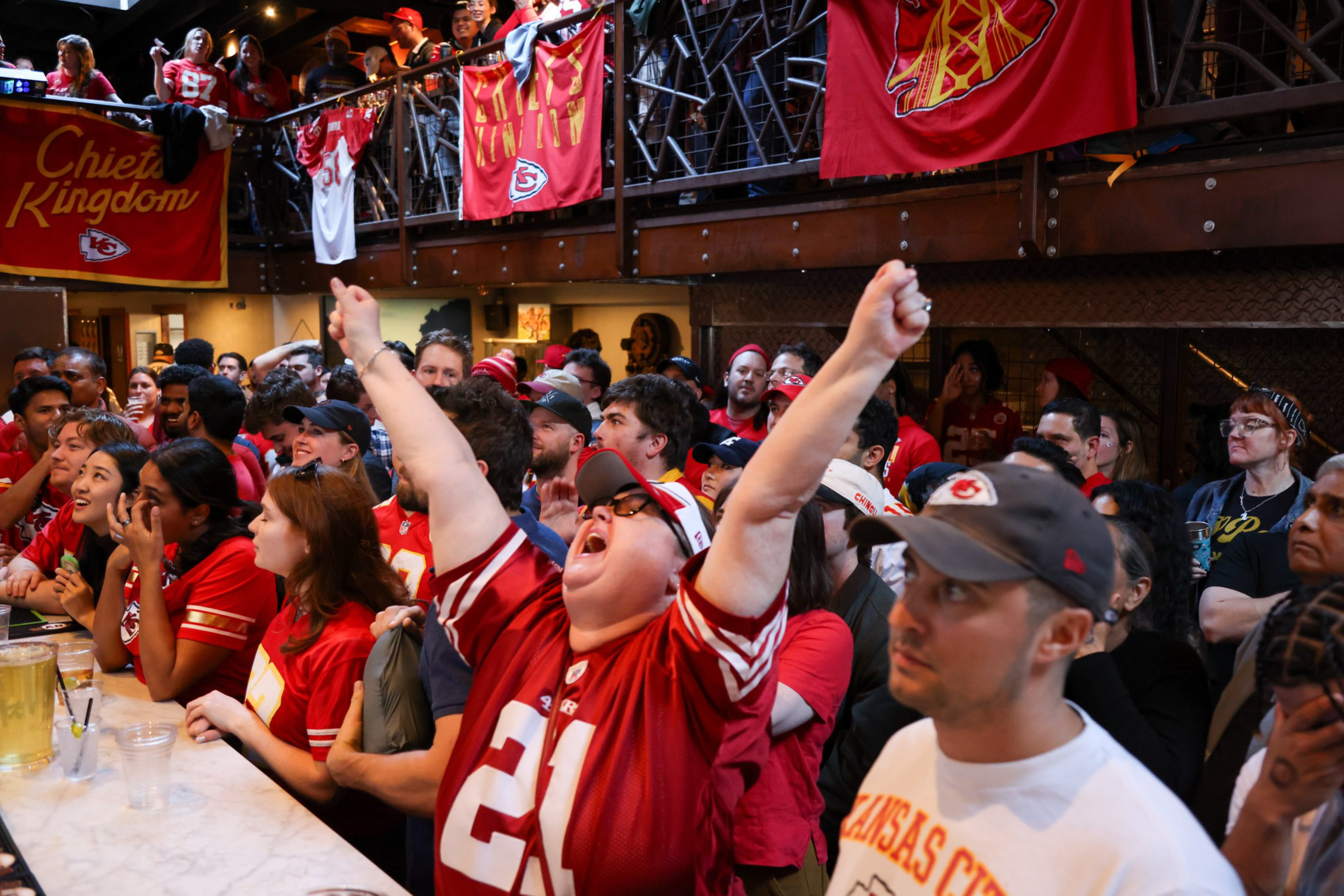 A crowd of excited fans in red jerseys cheering in a sports bar, with team banners above.