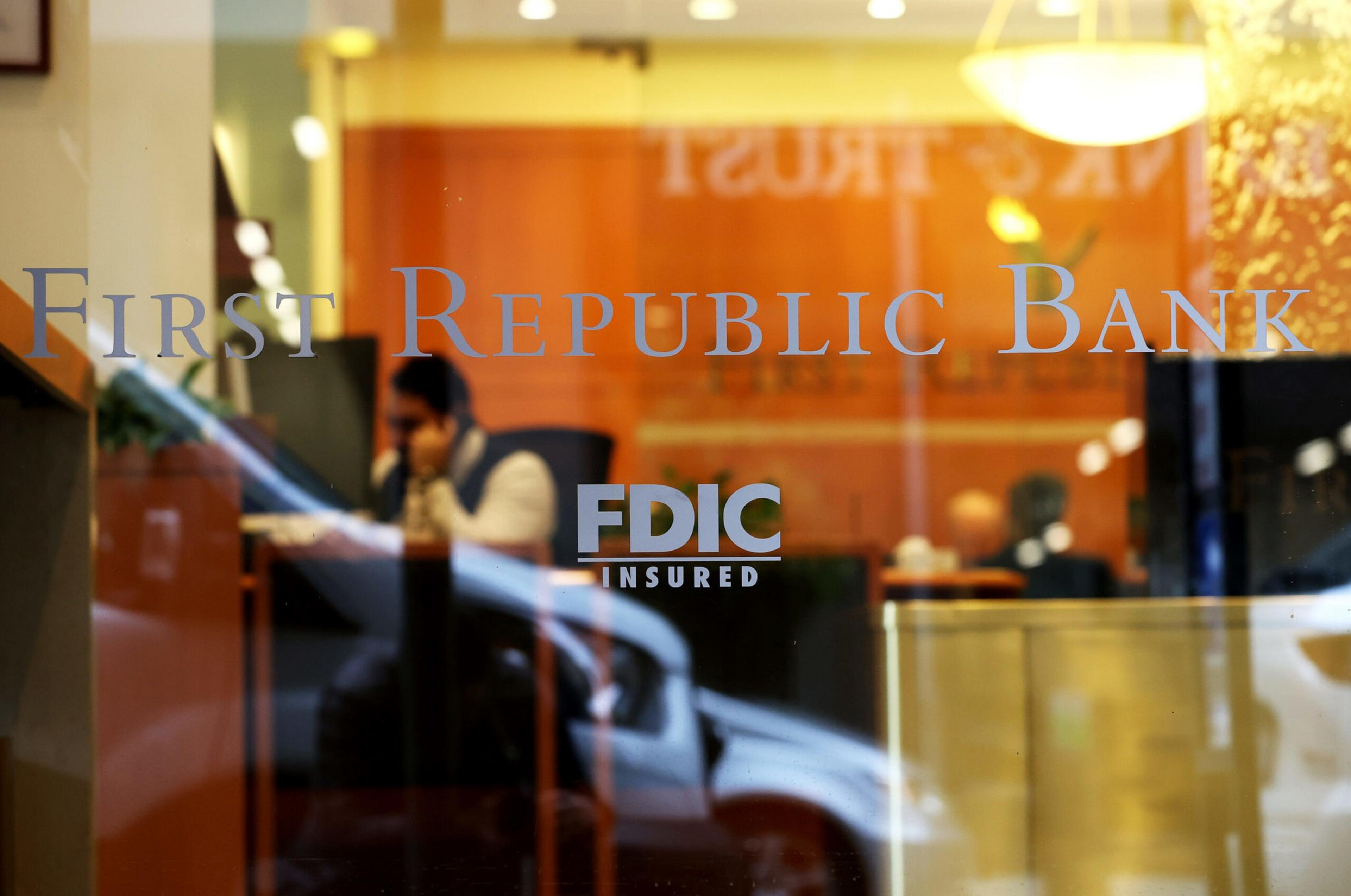 A person is blurred inside a First Republic Bank branch, visible behind glass with "FDIC Insured" marked on the window.