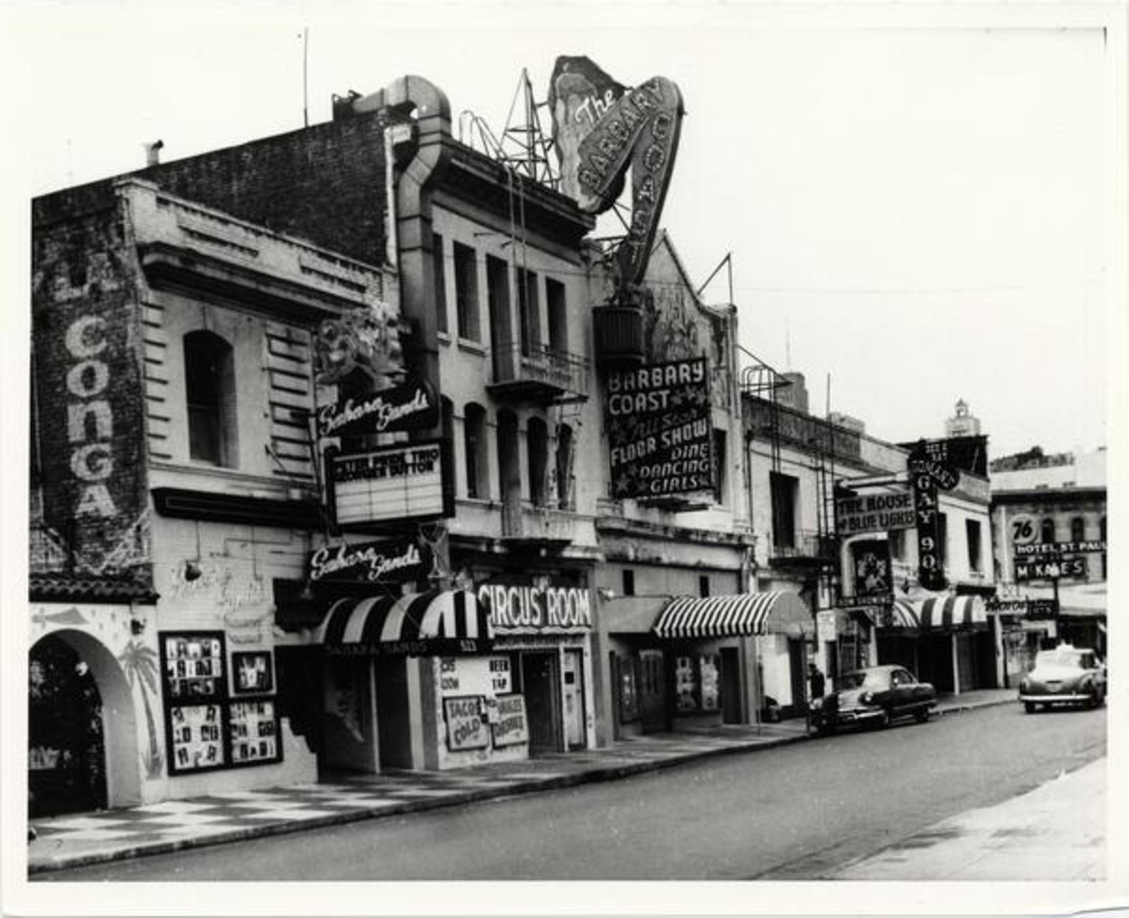 The image shows a vintage city street with old buildings, neon signs, and classic cars. The signs advertise various entertainment venues like nightclubs and theaters.