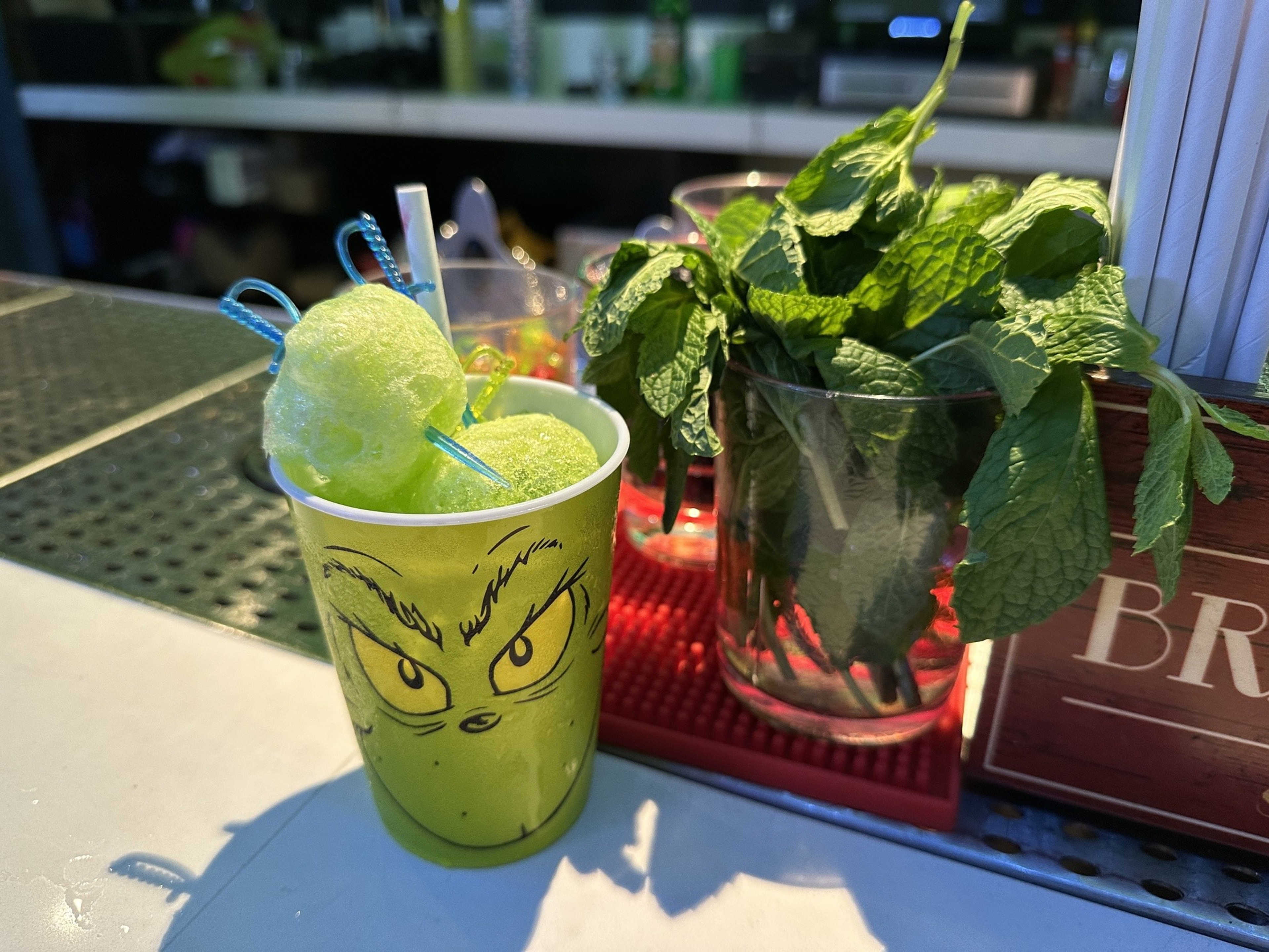 A lime green cocktail is served in a Grinch-themed cup with a puffy freeze-dried Jolly Rancher candy on top.