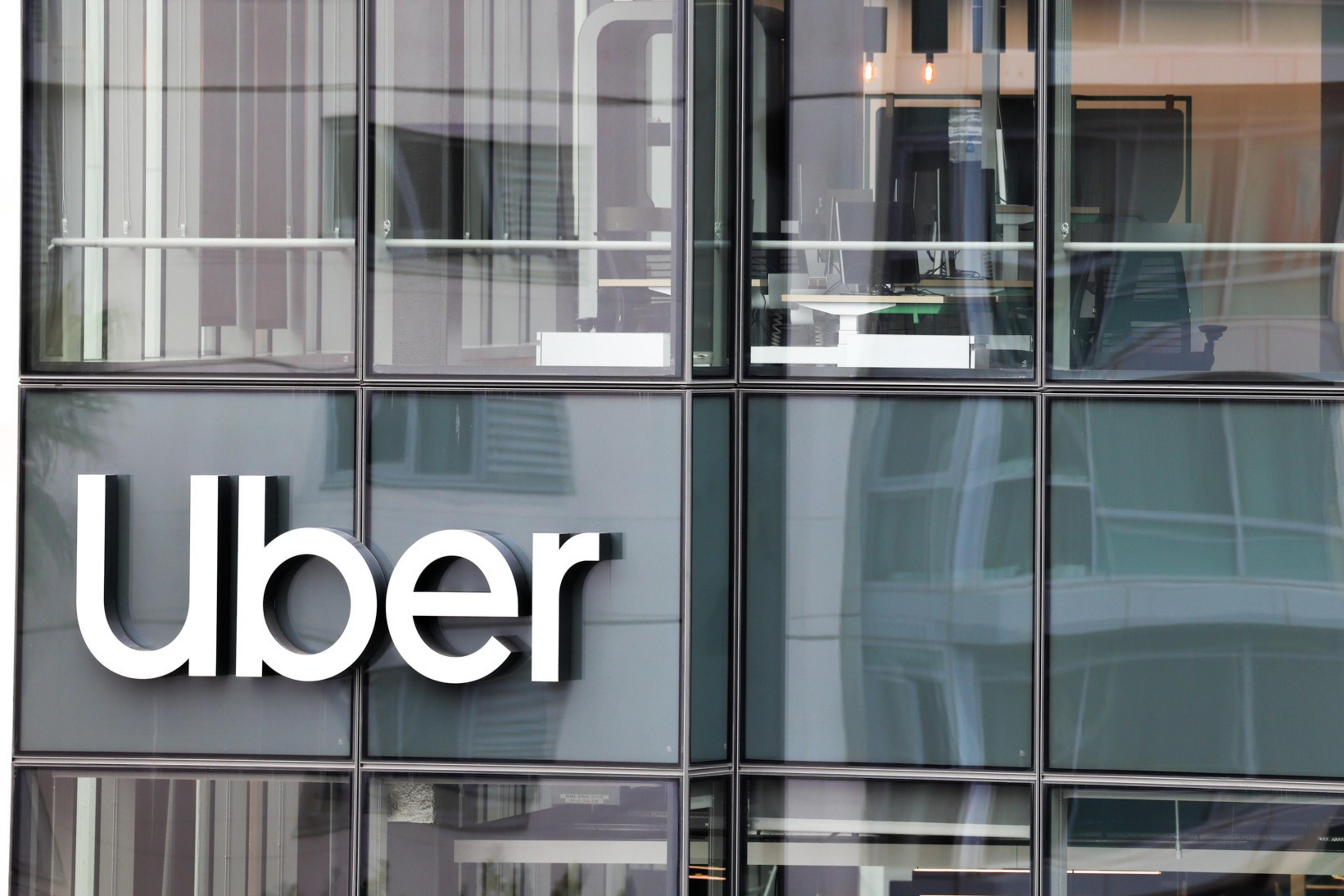 The image shows the large &quot;Uber&quot; logo on the exterior of a modern building with glass facade and reflections.