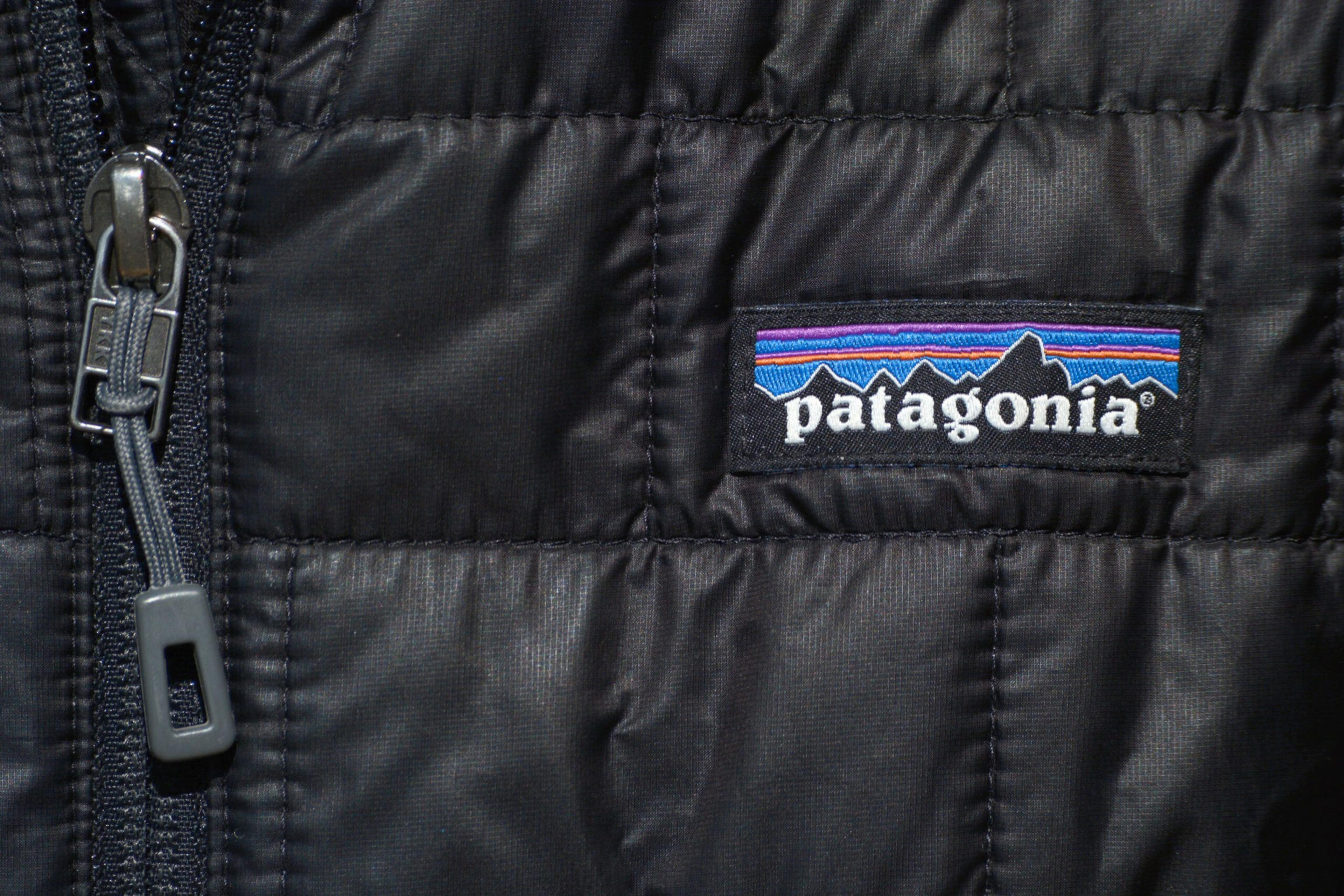 A close-up of a black quilted jacket with a zipper on the left side and a Patagonia logo patch featuring a mountain silhouette and colorful stripes.