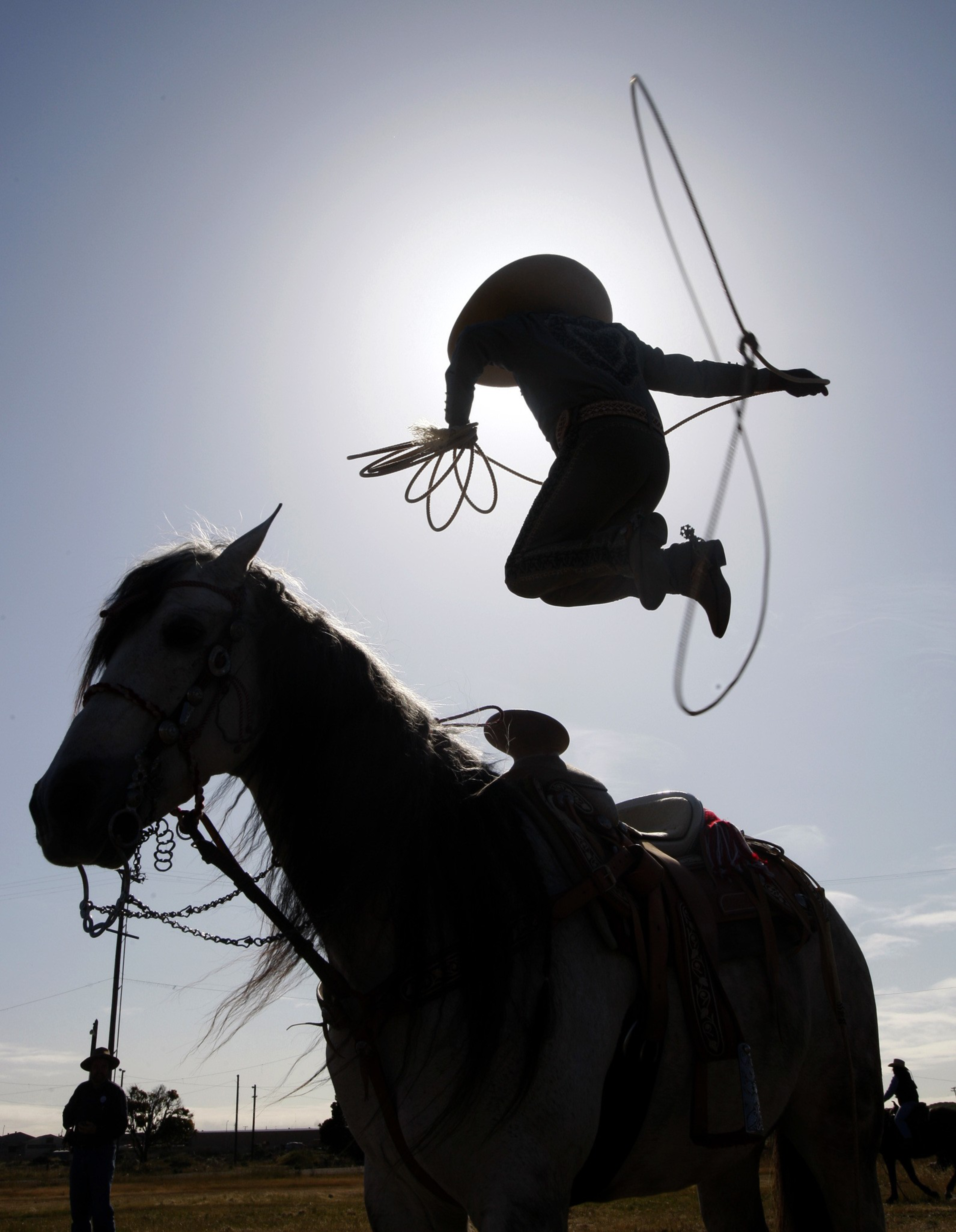 A silhouette of a person doing a trick on horseback with a lasso, backlit by the sun.