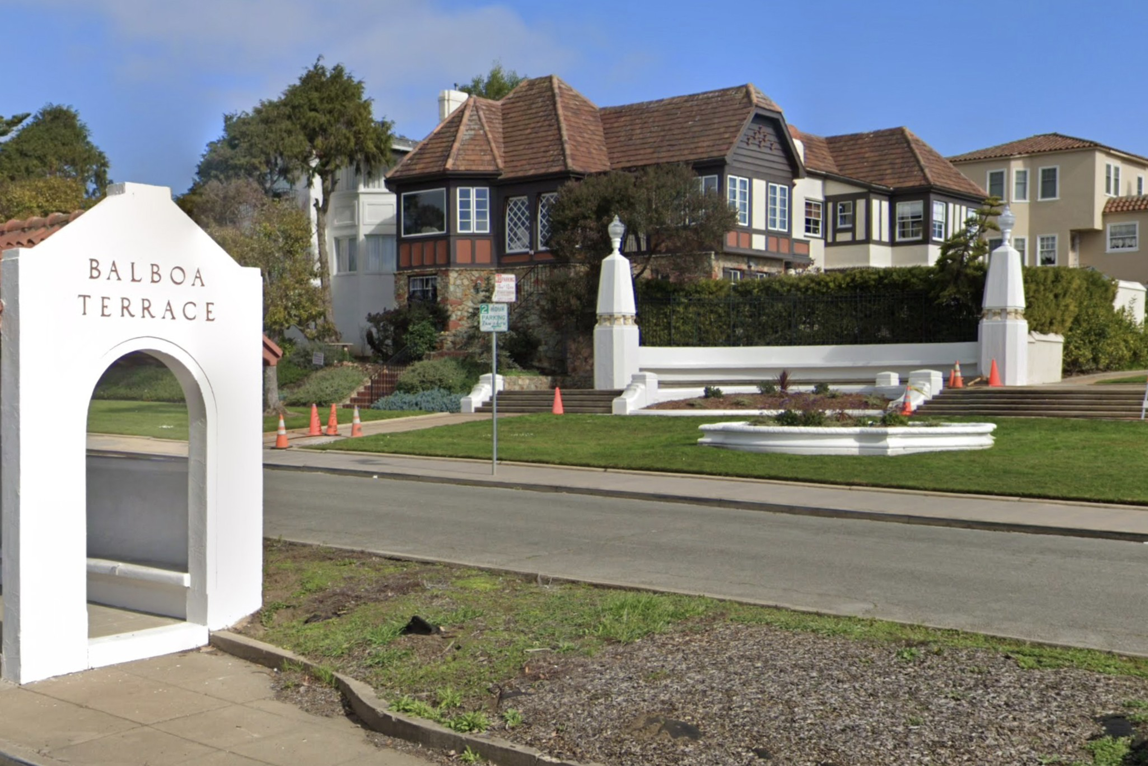 An arch reading &quot;BALBOA TERRACE&quot; with a fountain and Tudor-style homes behind it, under a clear sky.
