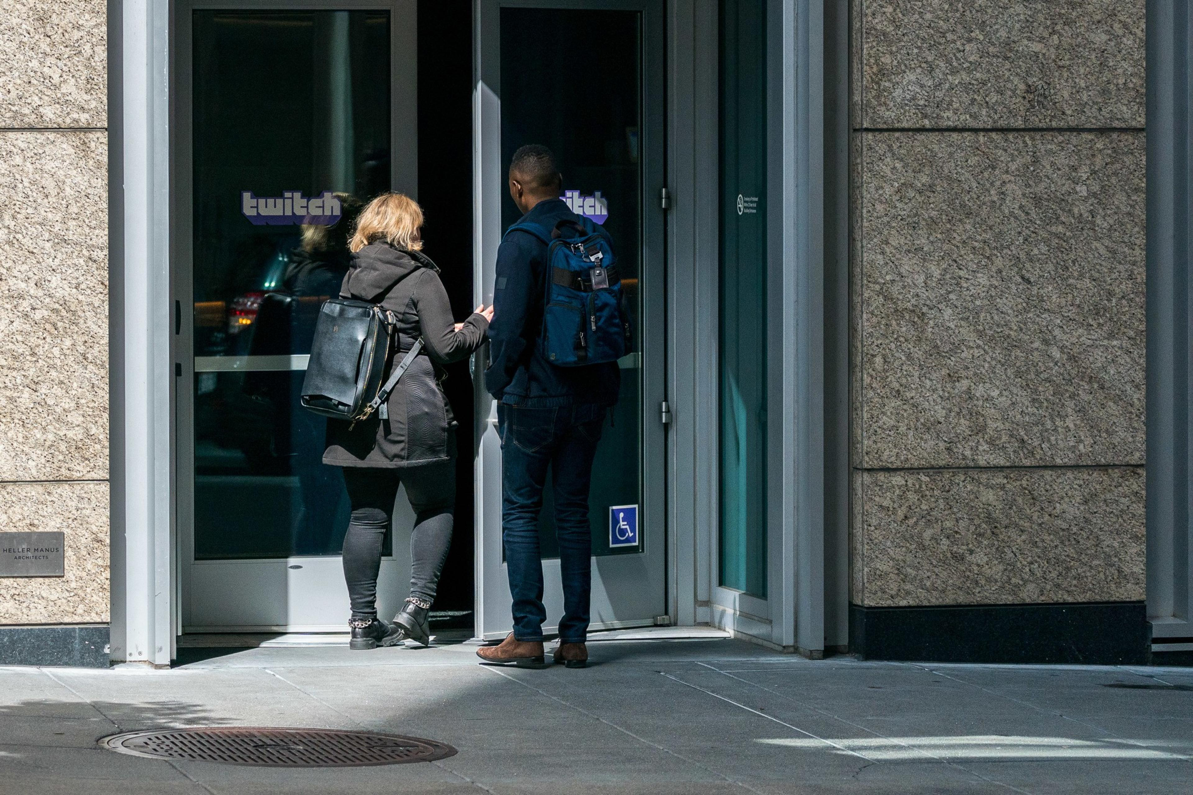 Two people are entering a building with a "Twitch" logo on the door.