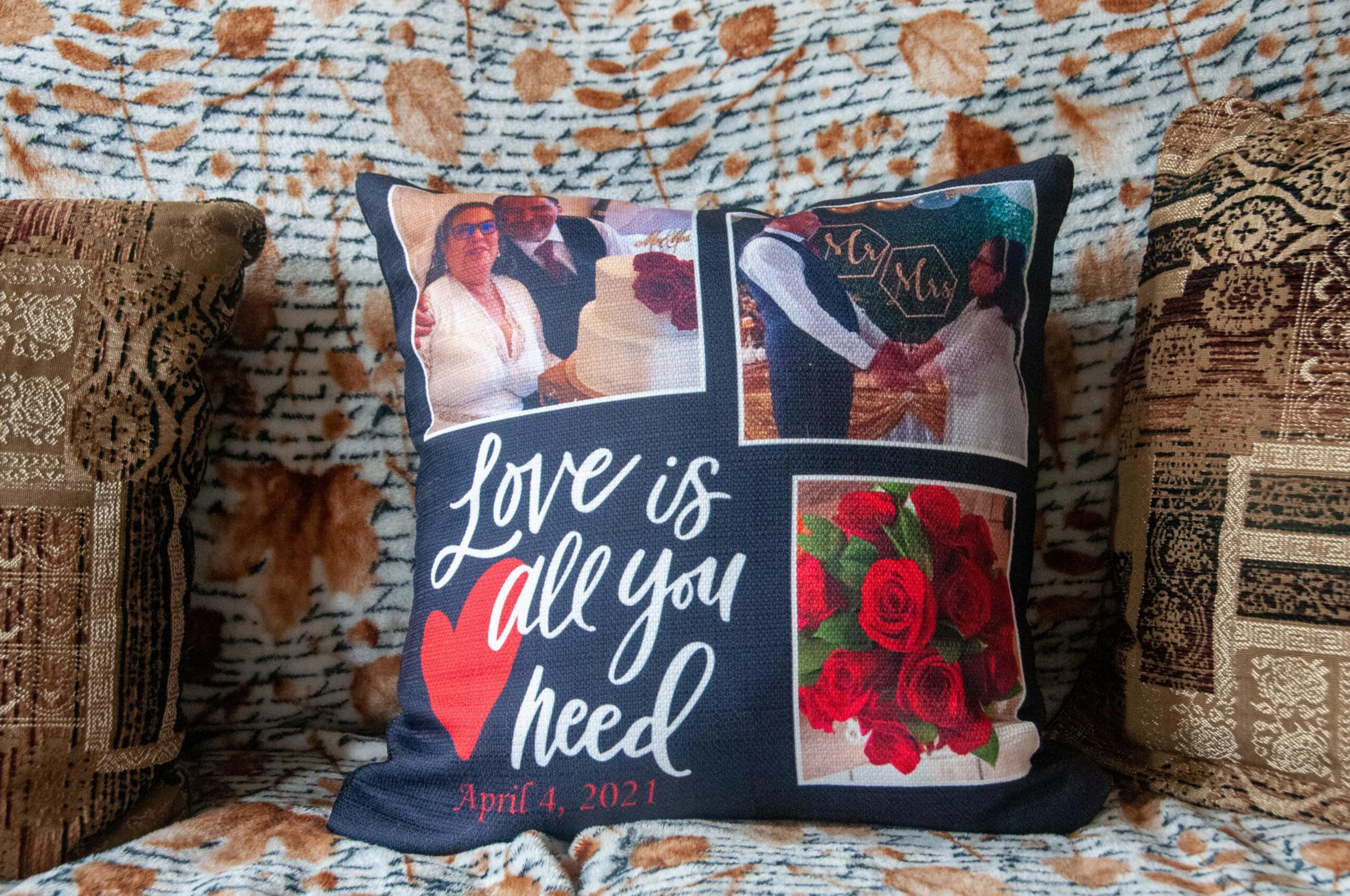 A decorative pillow with three photos—a wedding couple cutting cake, holding hands, and a bouquet of red roses—with the text "Love is all you need" and the date April 4, 2021.